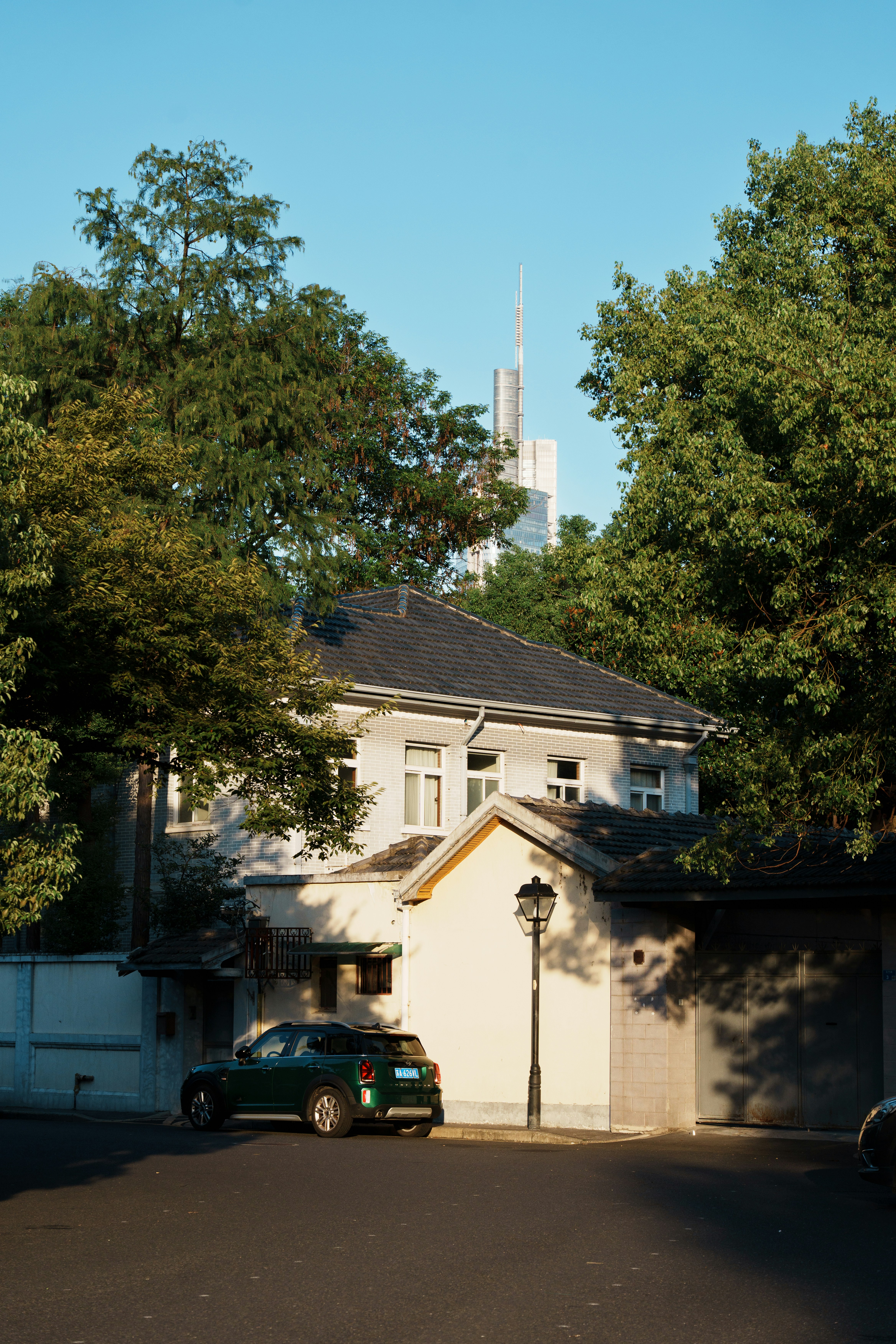 A green car parked on a street before a house with a skyscraper behind