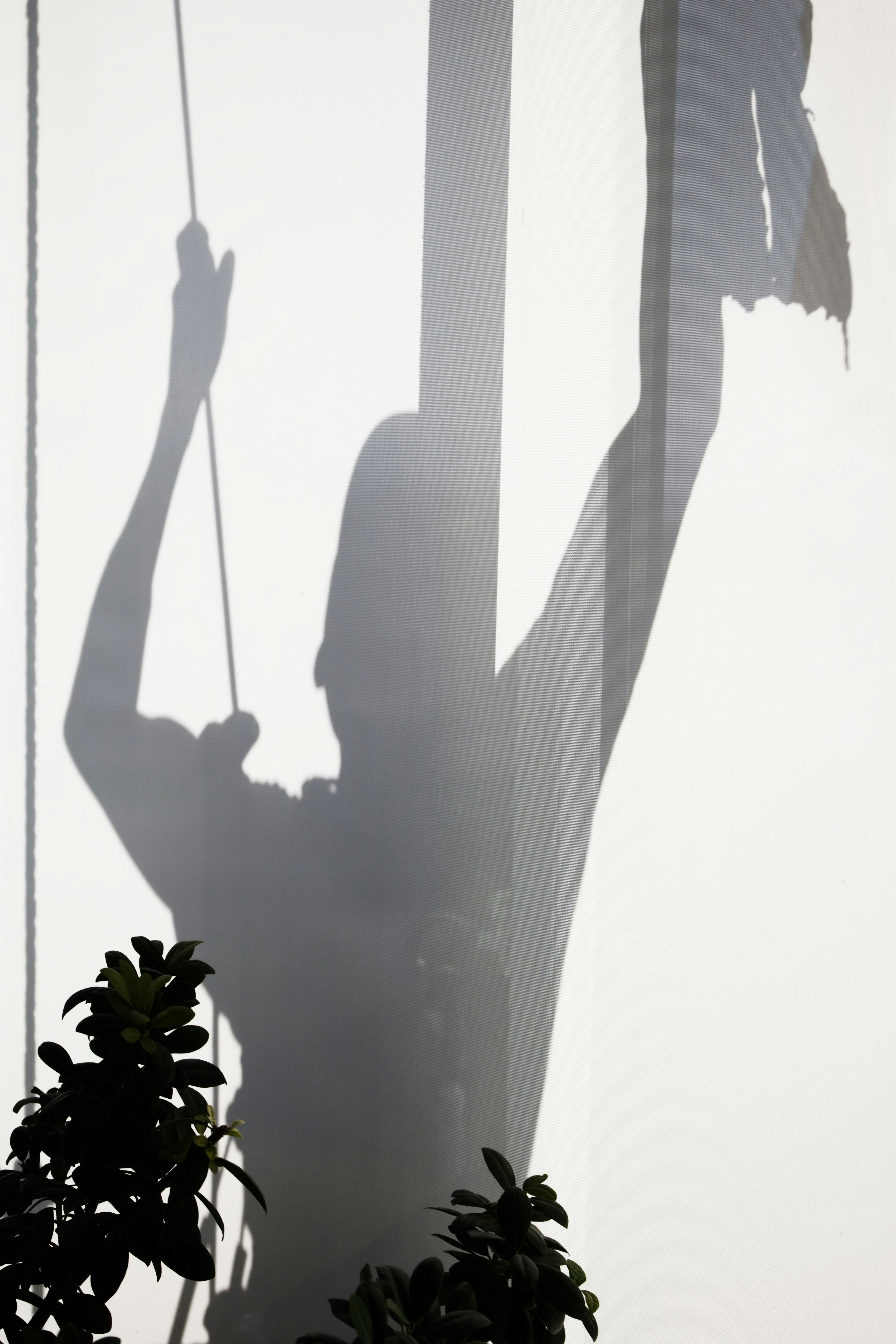 A silhouette of a person pulling a cord against a white curtain