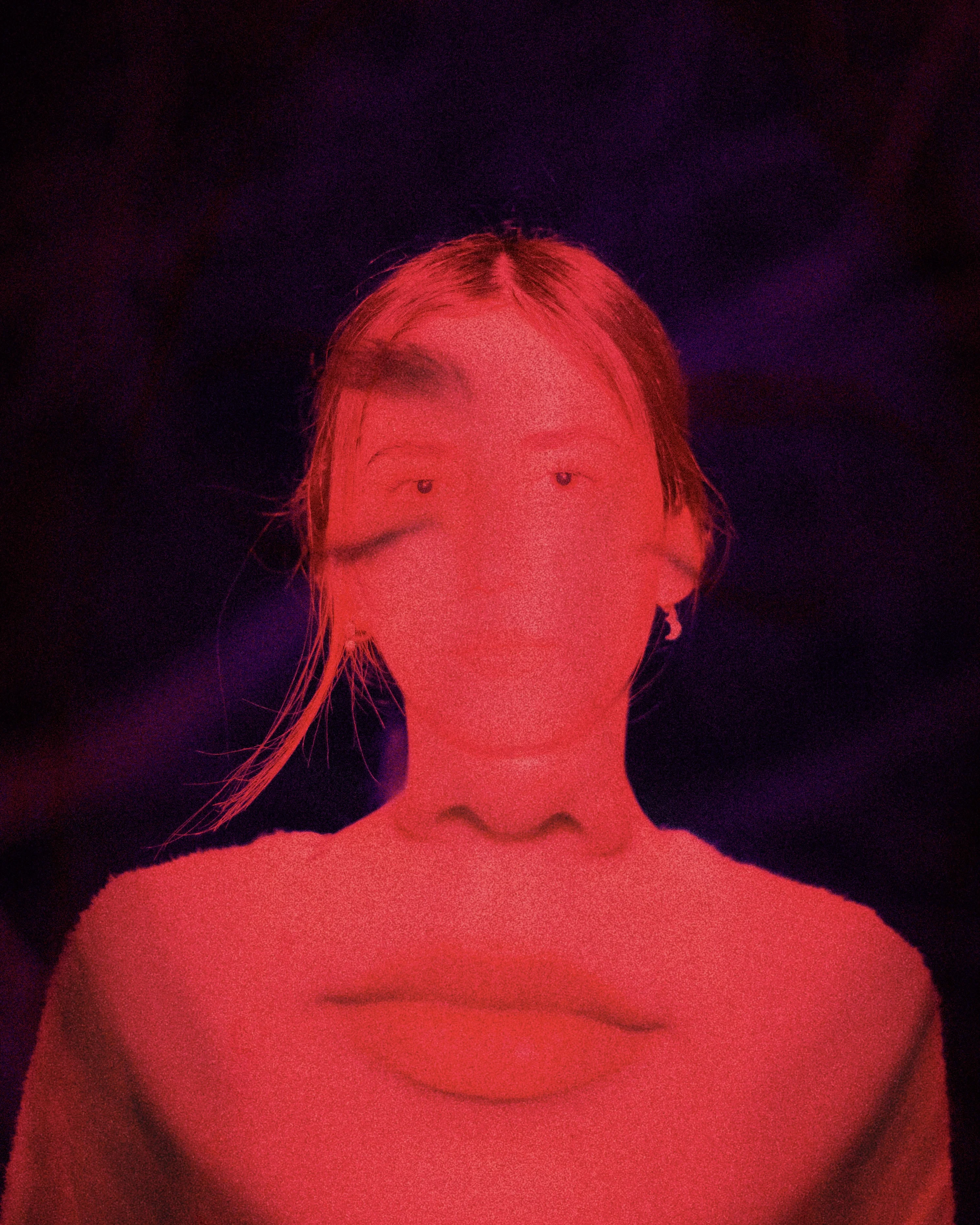 A person with long hair in bright red light against a dark background
