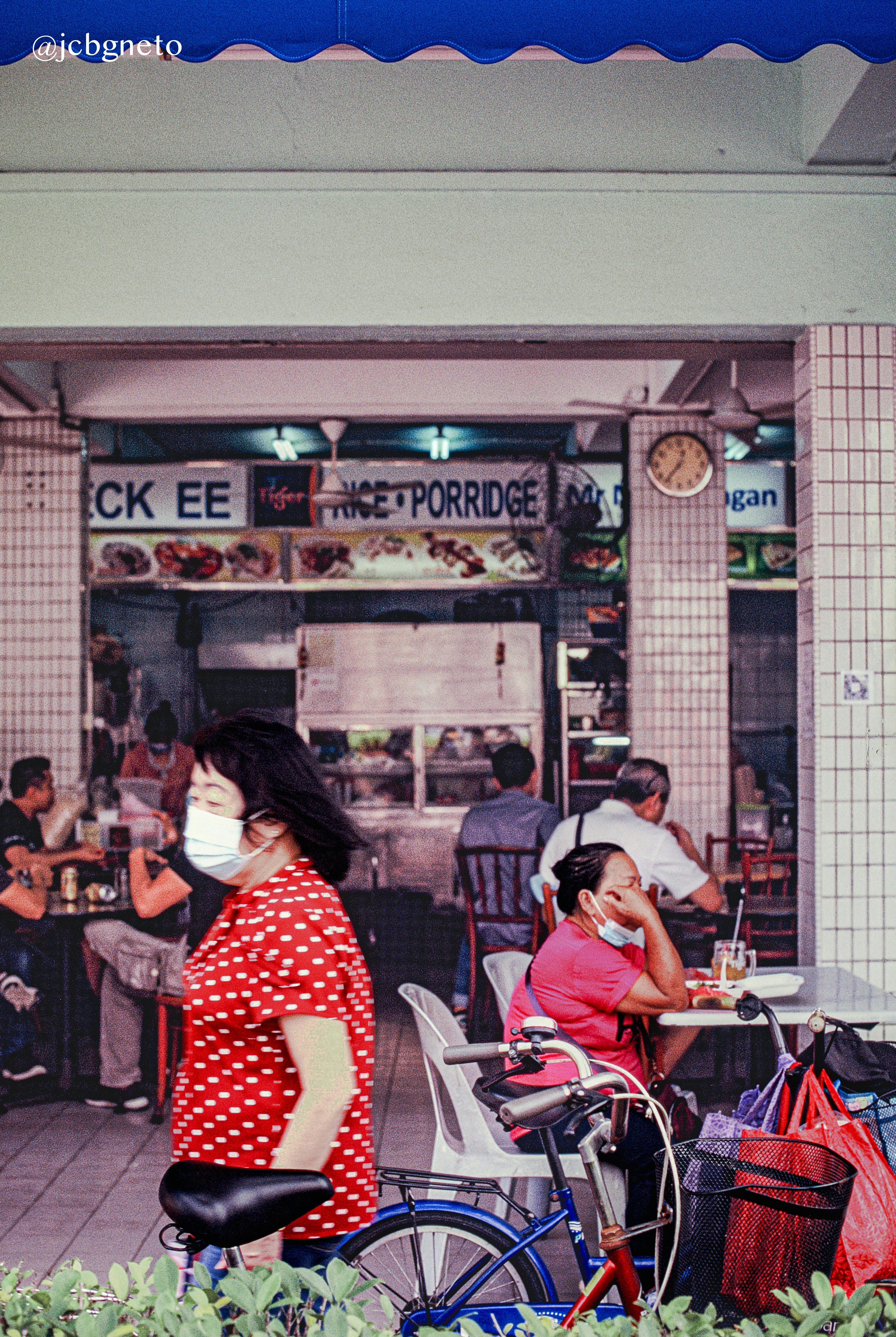 A woman in a red polka dot shirt walking past an outdoor food stall