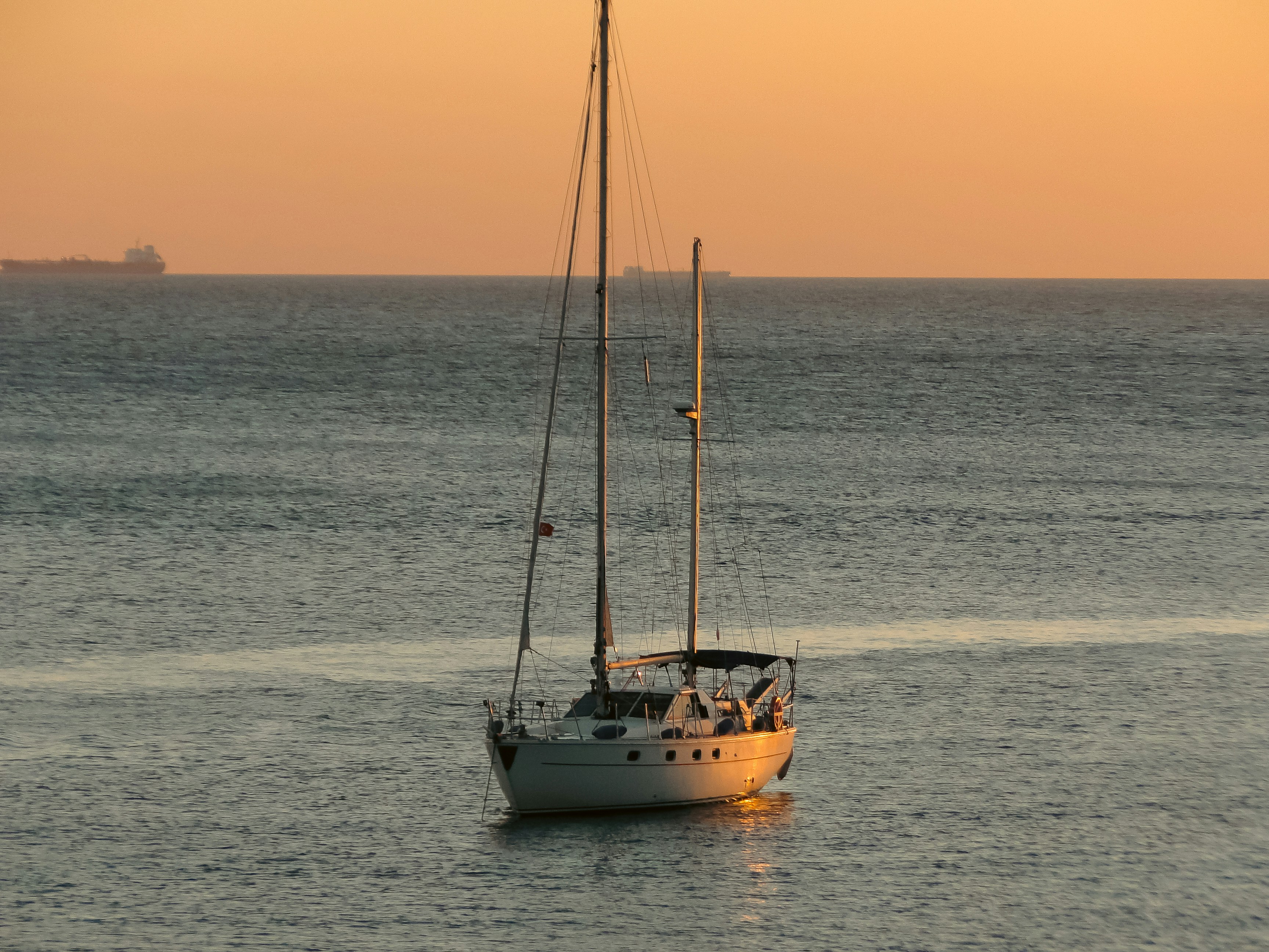 Un velero en aguas tranquilas bajo un cálido cielo naranja bajo sol bajo