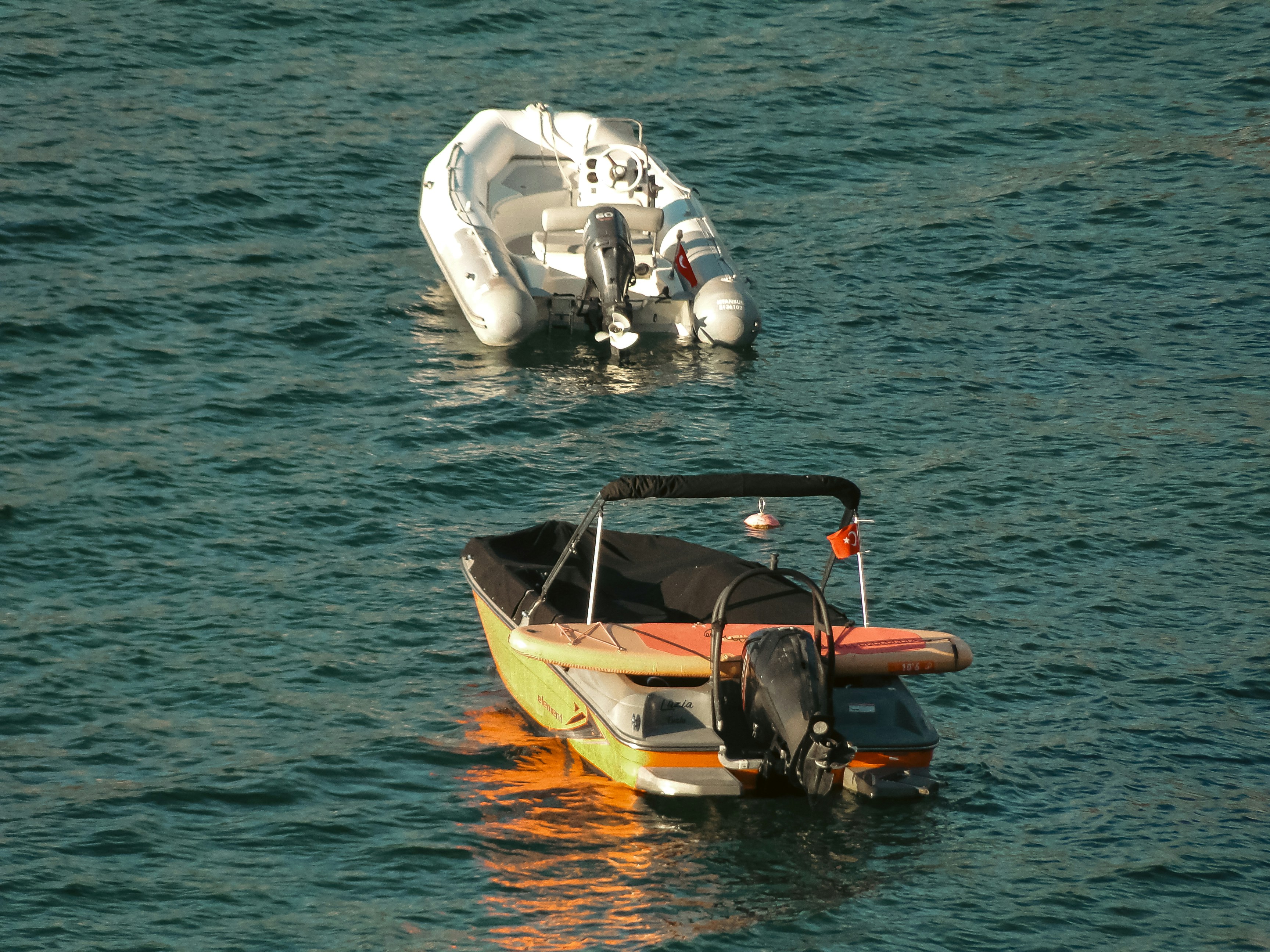 Una embarcación inflable blanca y una pequeña lancha motora con tabla de paddle sobre aguas azules
