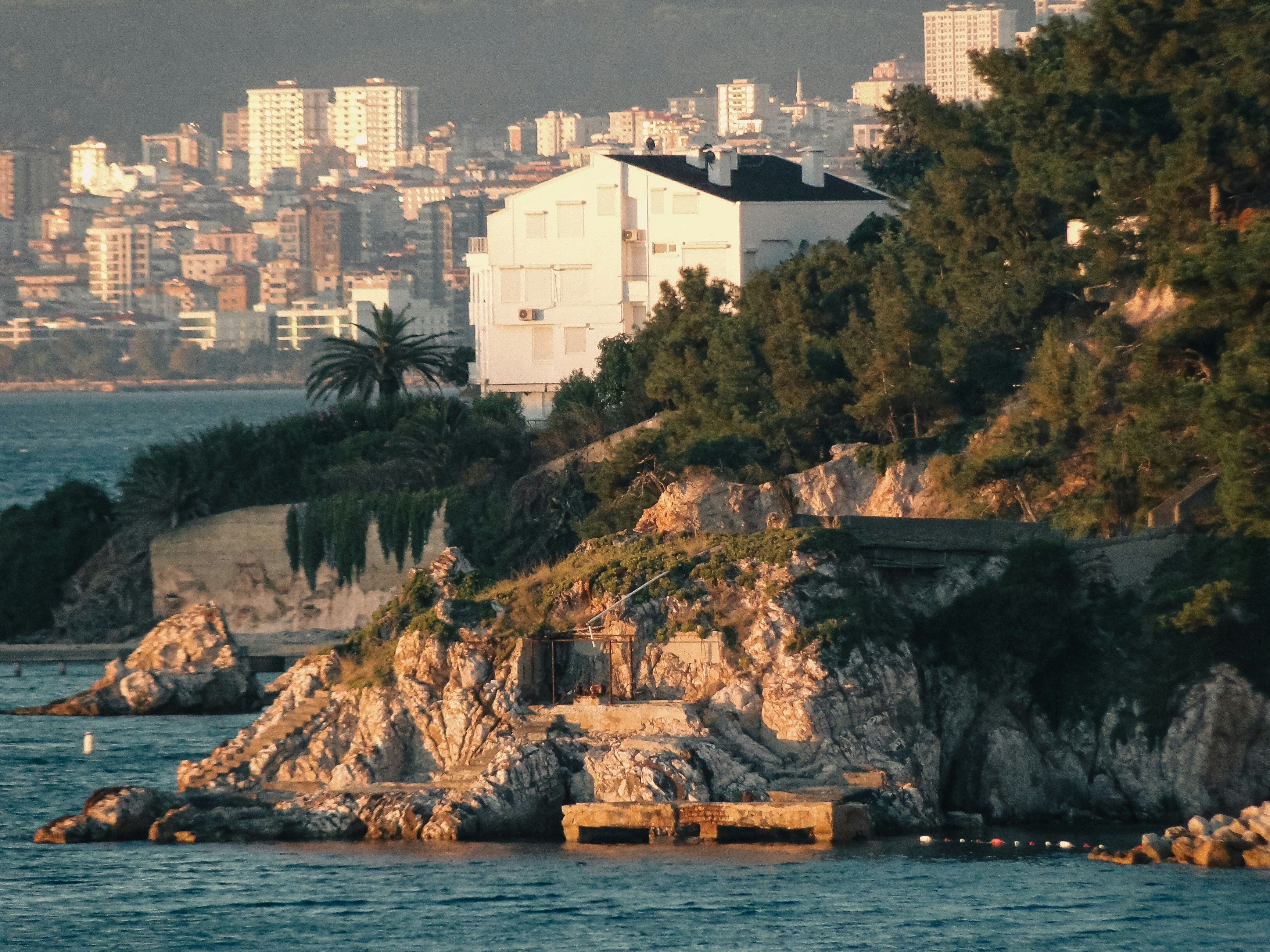 Una casa blanca en una costa rocosa con una ciudad de fondo