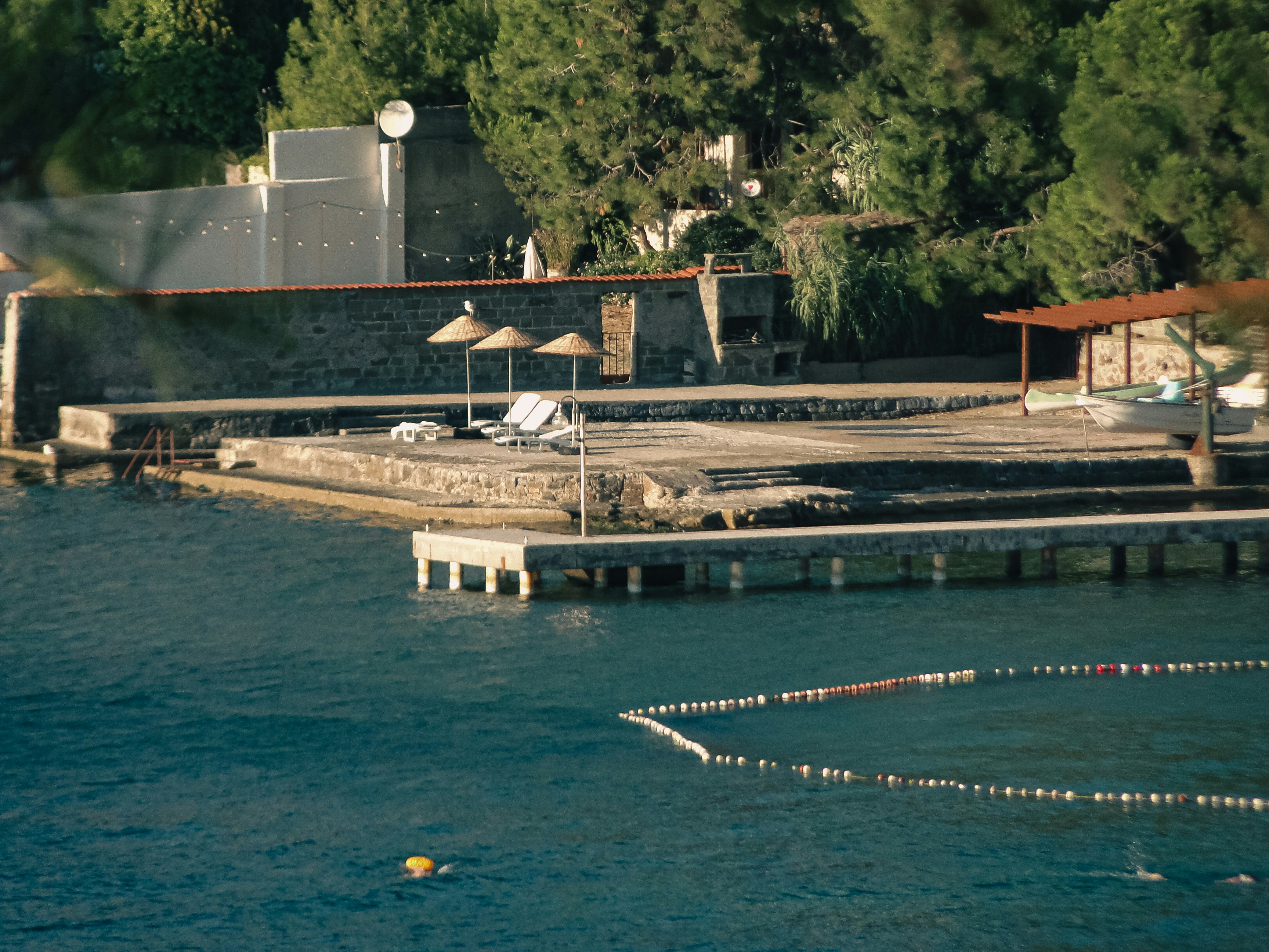 Un muelle de piedra con tumbonas y sombrillas junto a un mar azul tranquilo