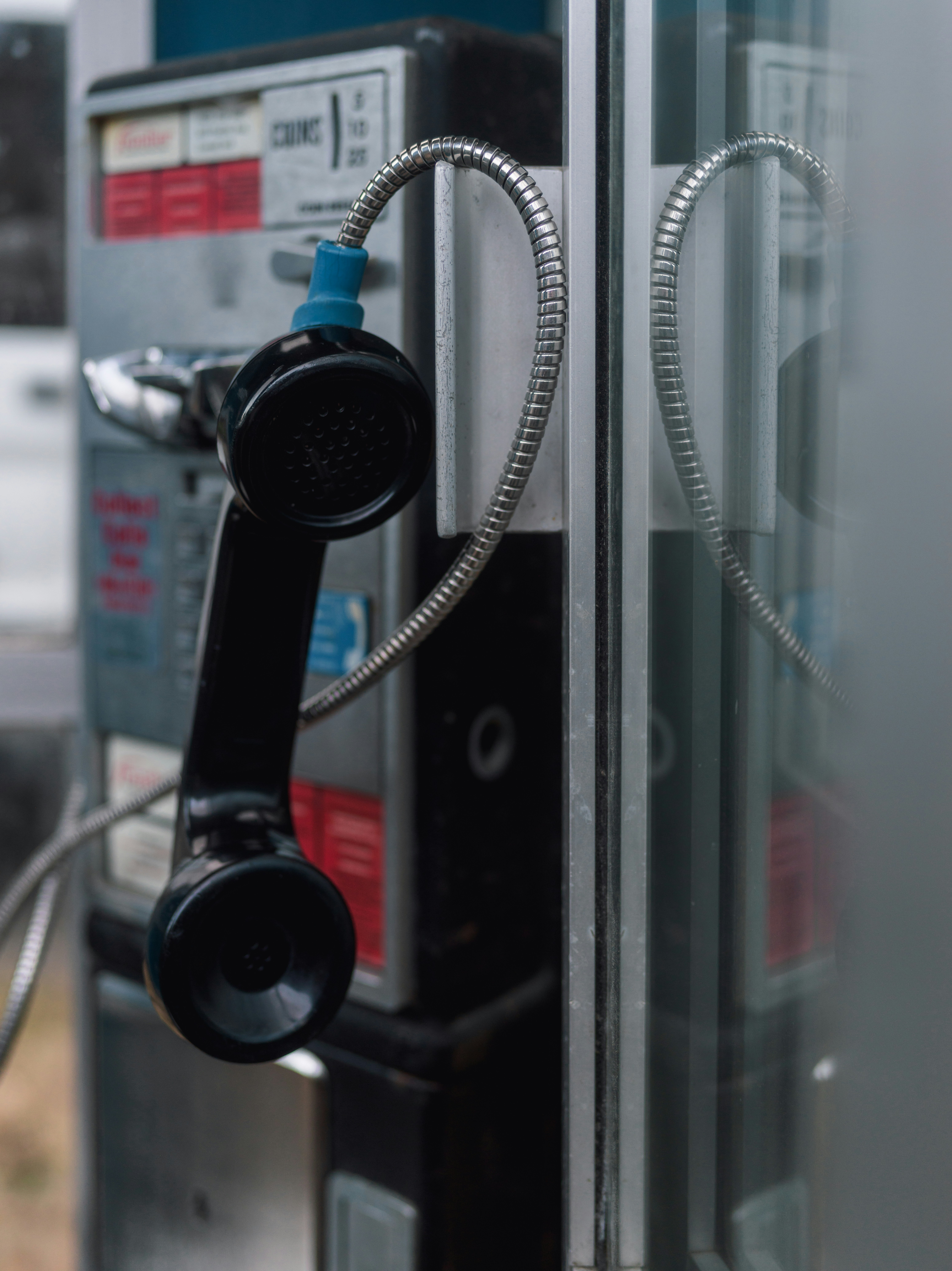 A black telephone handset hanging by a metal cord from a public booth