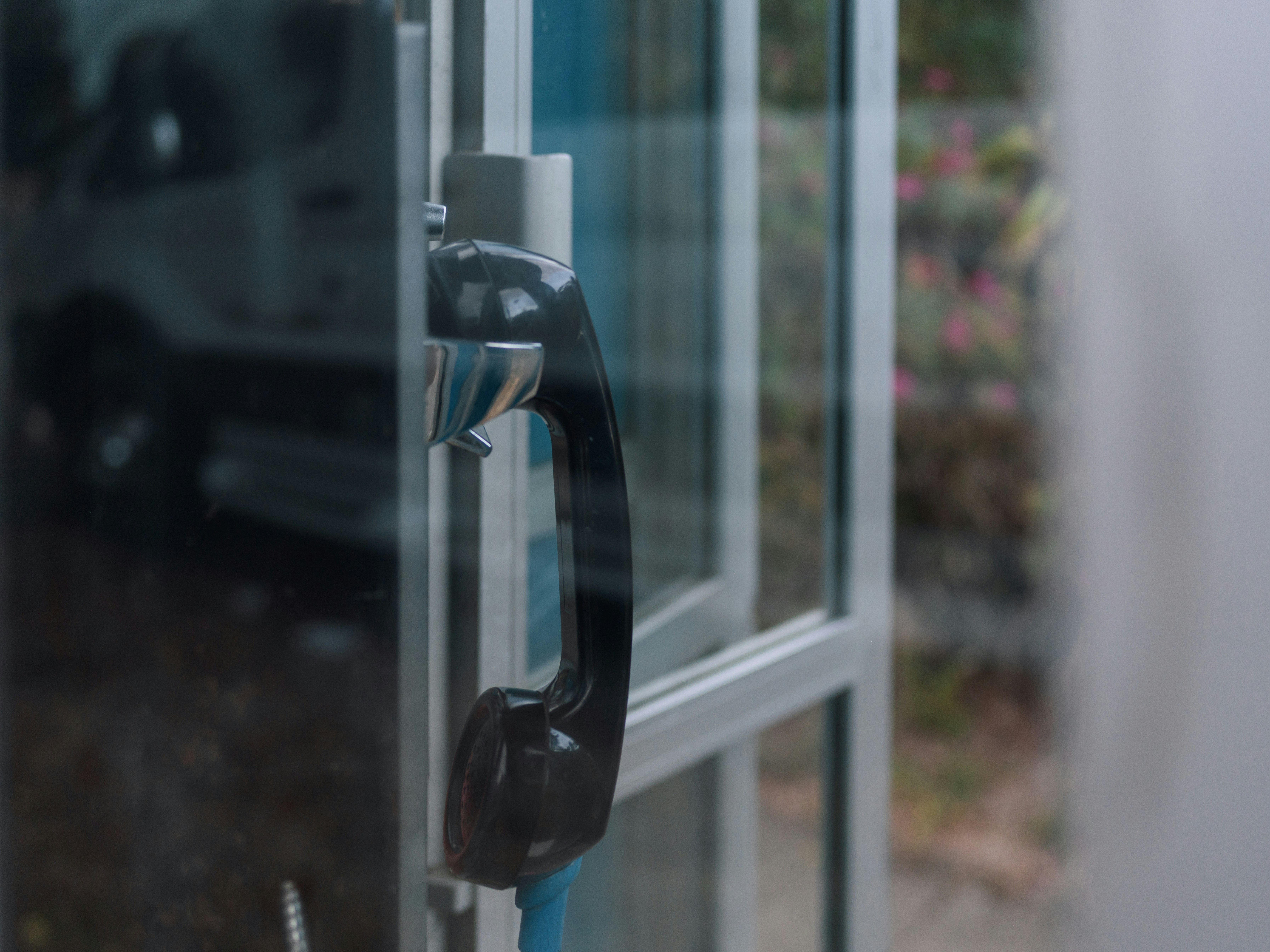 A black telephone handset hanging inside a glass phone booth
