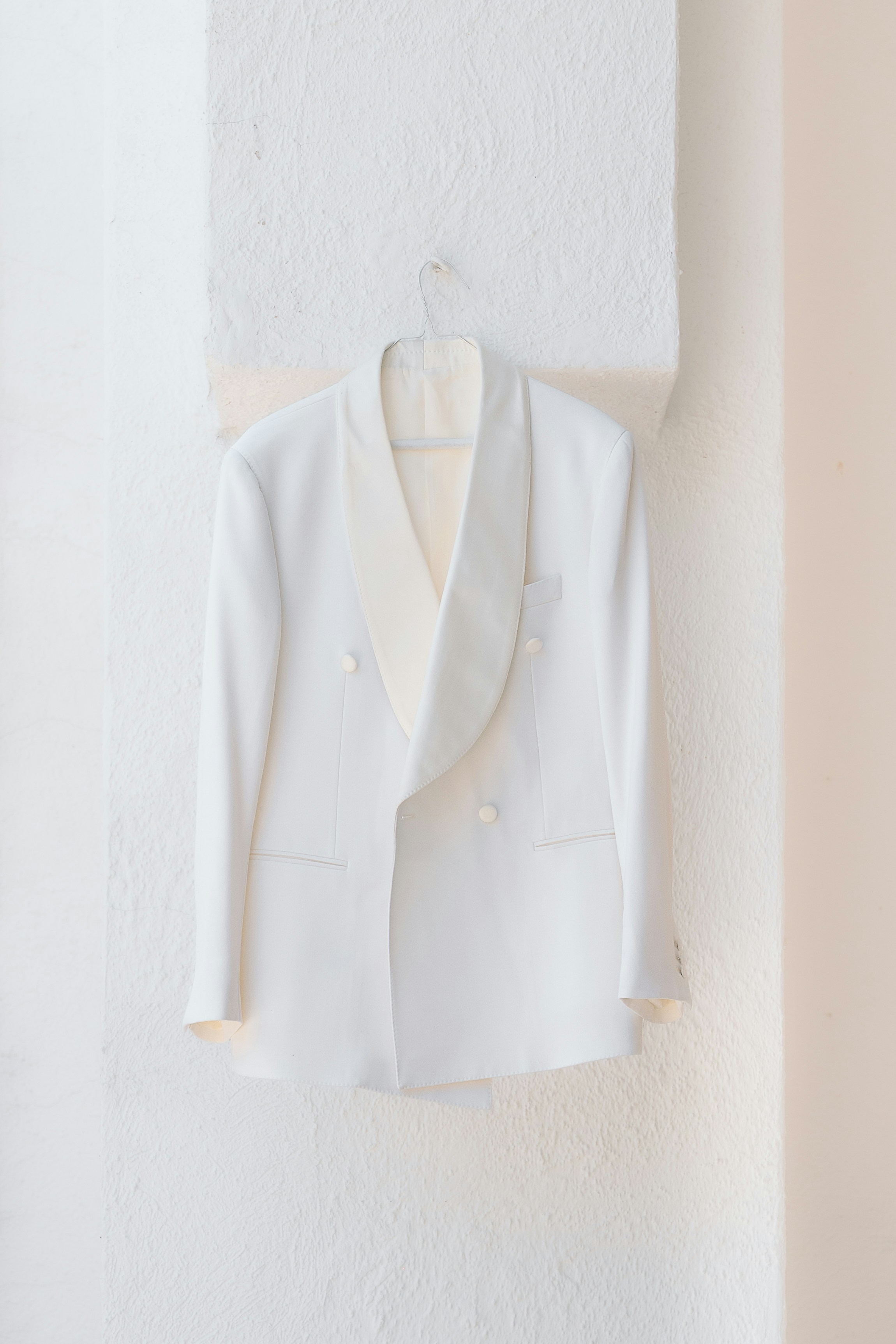 A white double-breasted tuxedo jacket hanging on a wire hanger against a wall - 相关推荐
