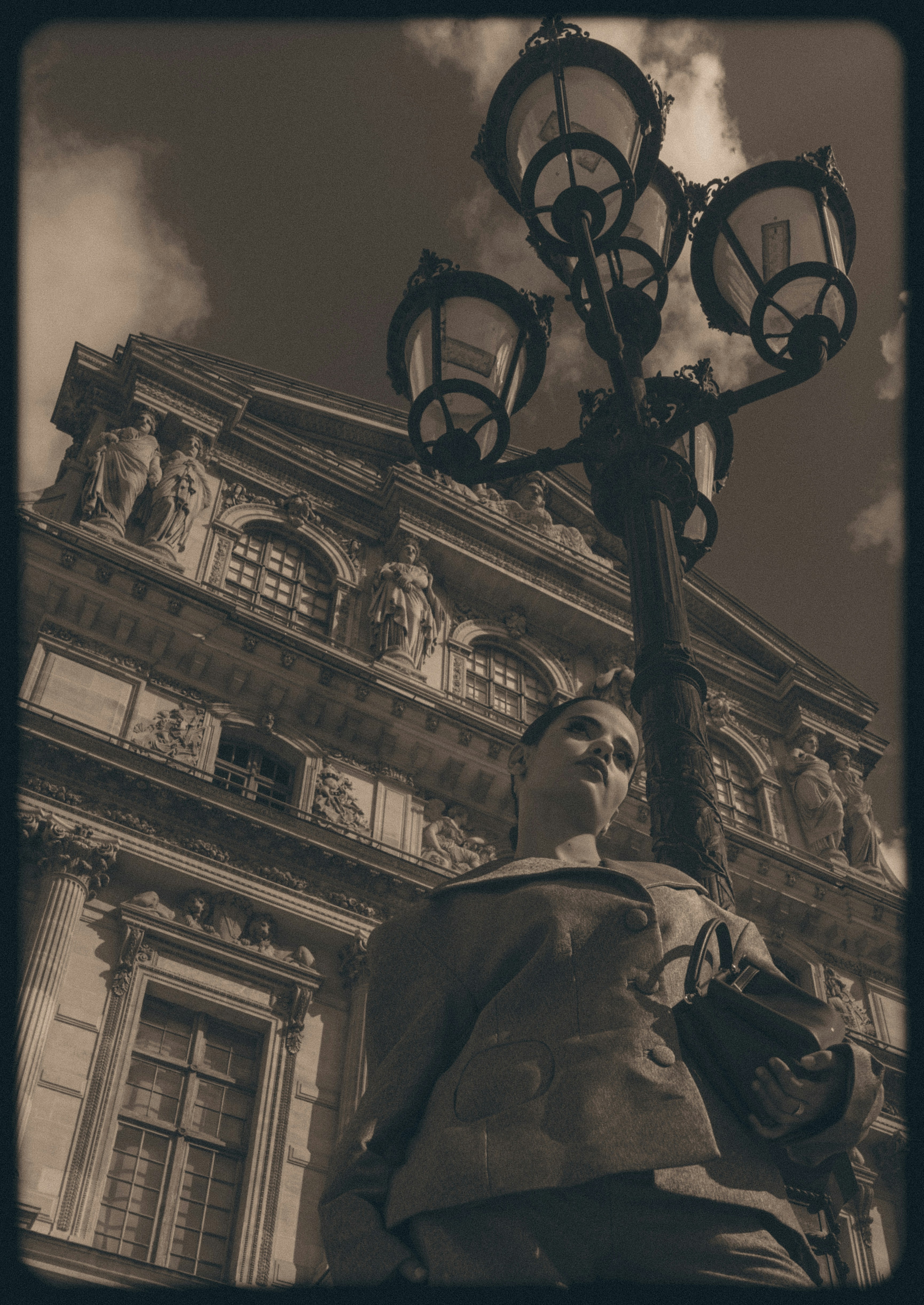 A person in a coat holding a handbag beside an ornate street lamp