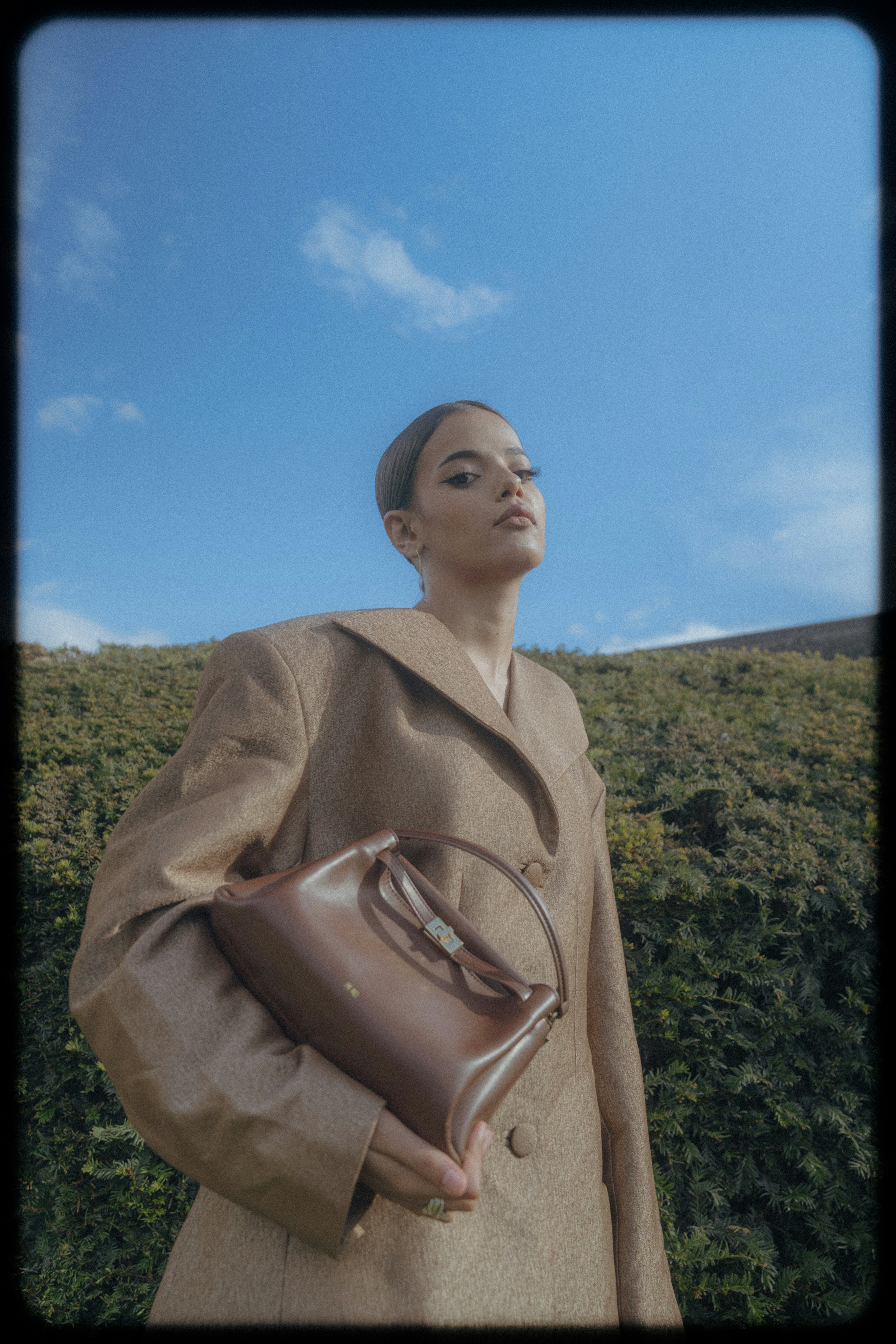 A woman in a tan blazer holding a brown leather handbag outdoors