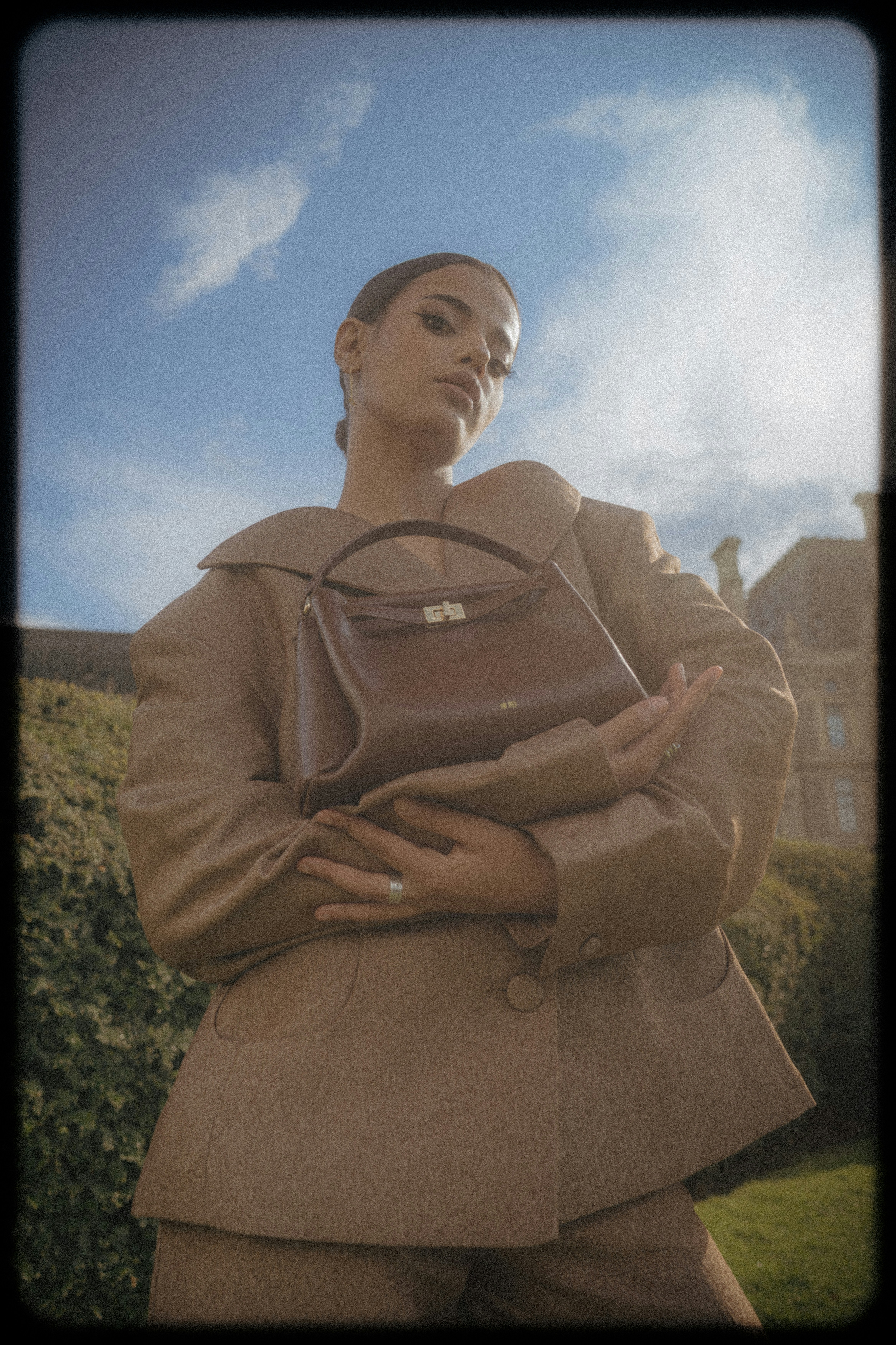 A woman in a tan blazer holding a brown leather handbag outdoors