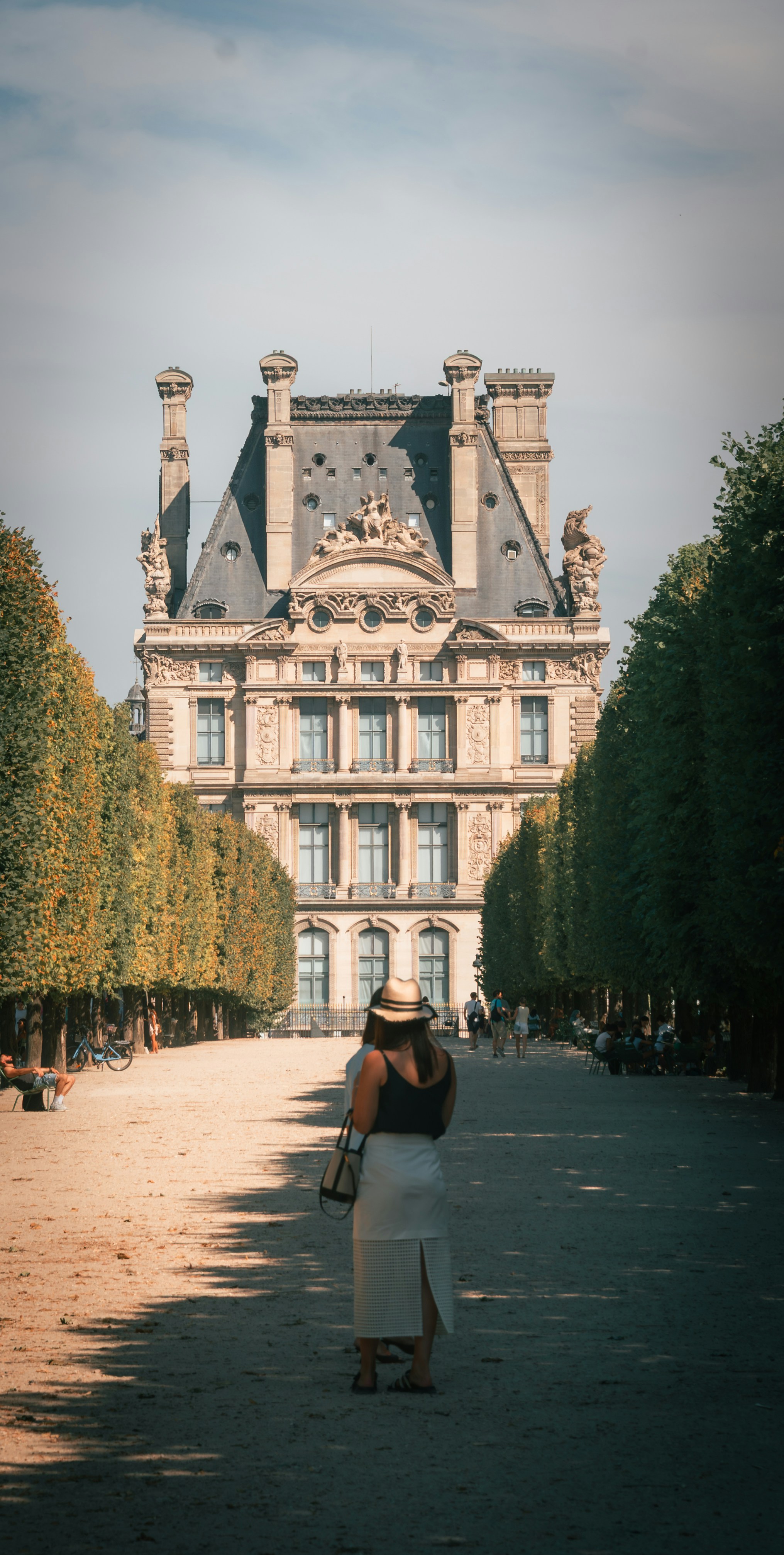 A woman in a hat walking toward the Louvre Palace in Paris