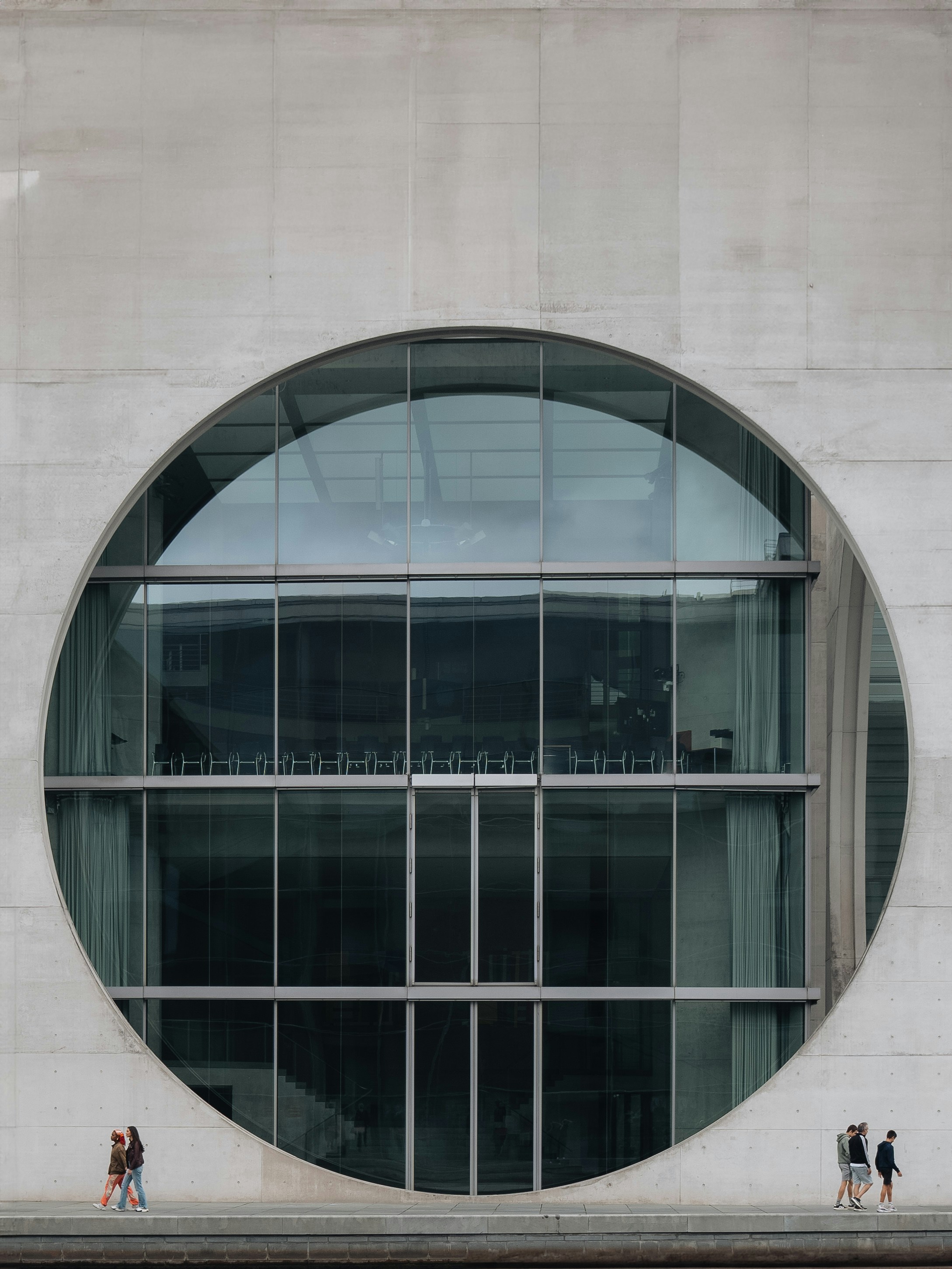 People walking on a concrete path in front of a large circular glass window
