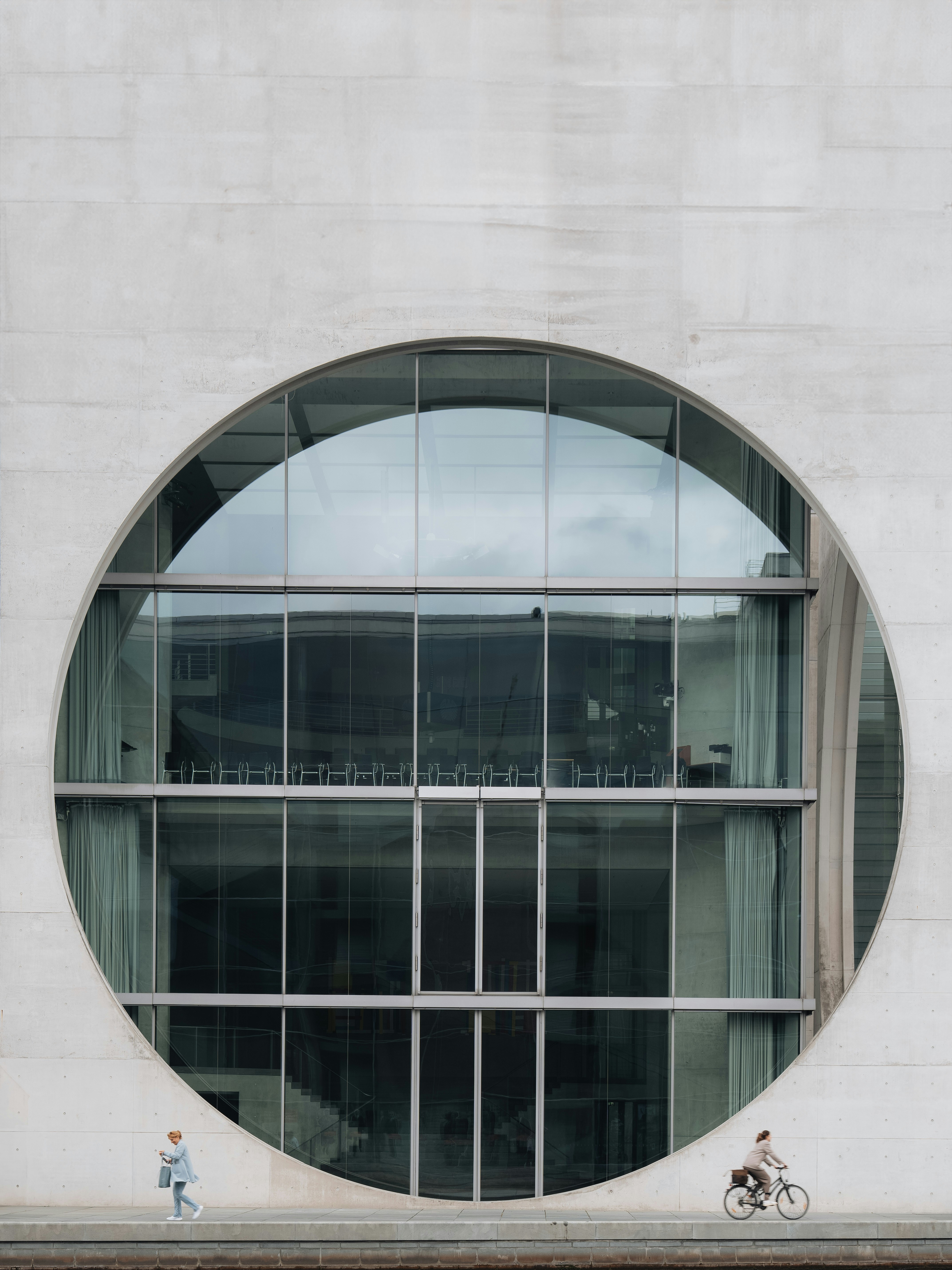 A person walking and a person cycling past a large circular glass window