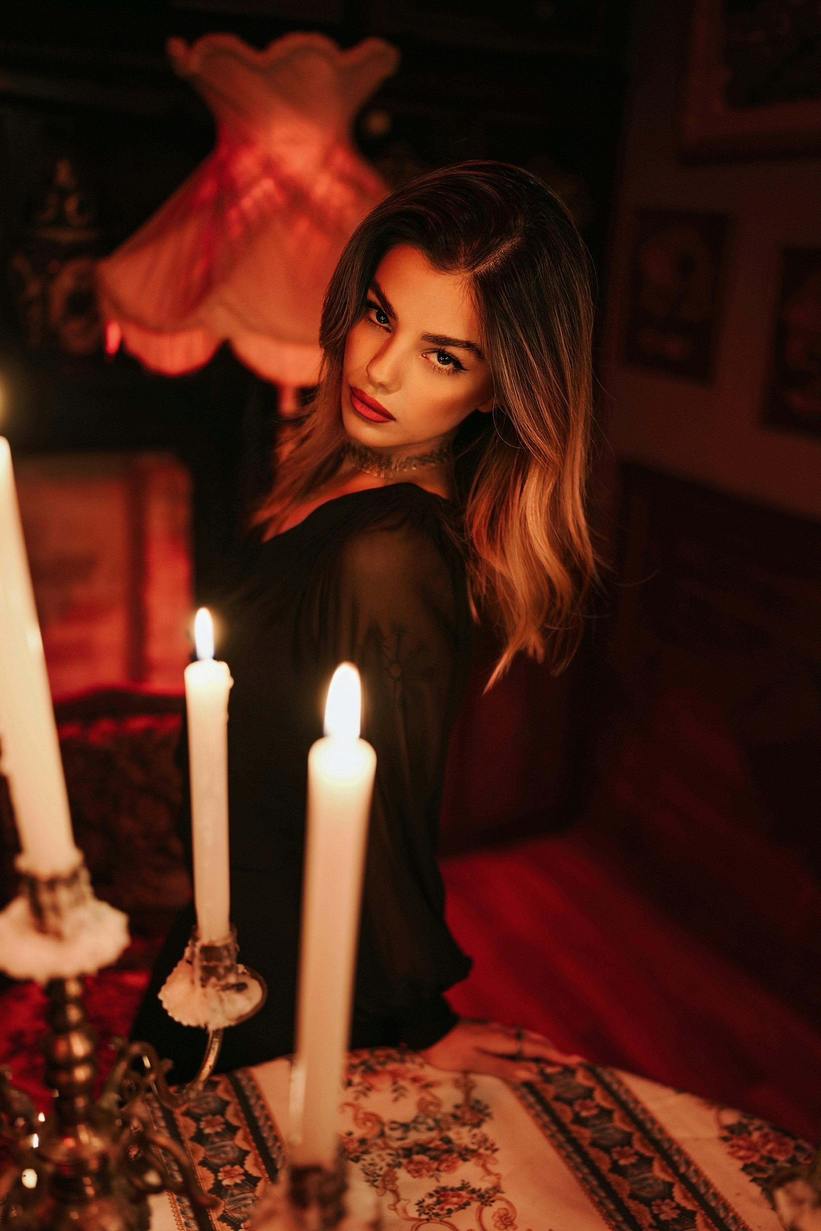 A woman in a black dress beside lit candles in a dimly lit room