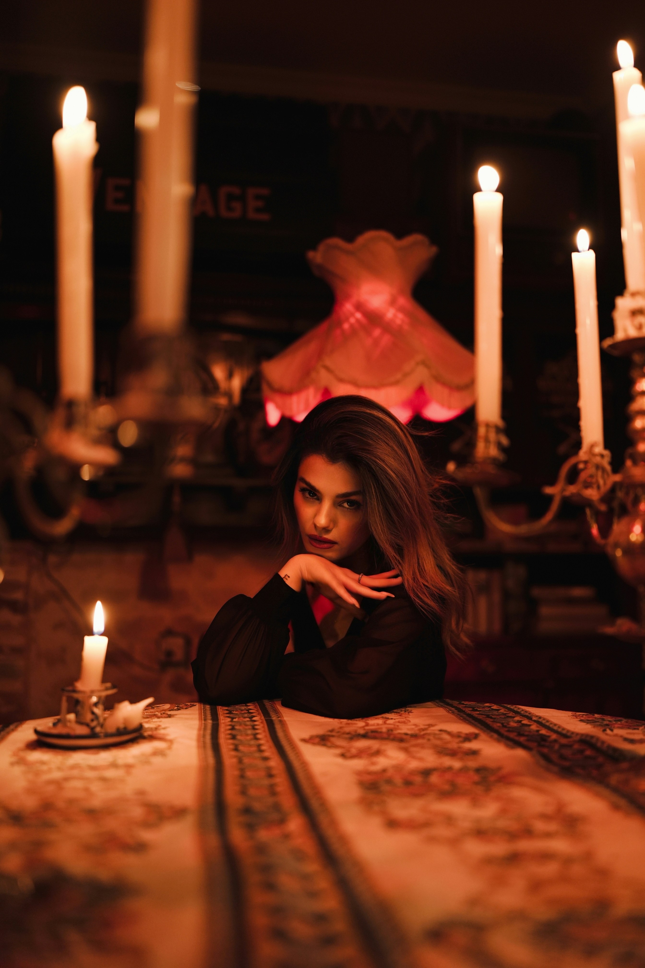 A woman in a black top resting her chin on her hand by candlelight