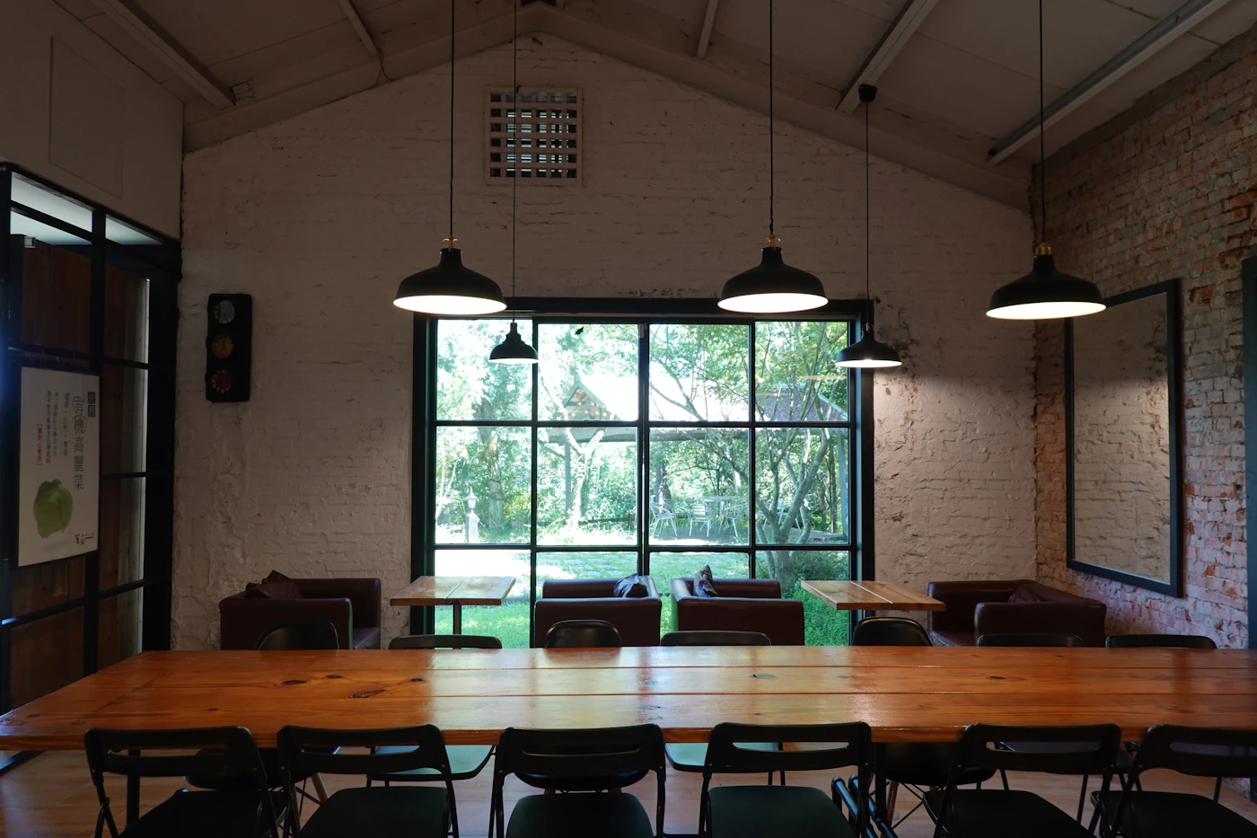 A long shared table under pendant lights in a brick-walled common room