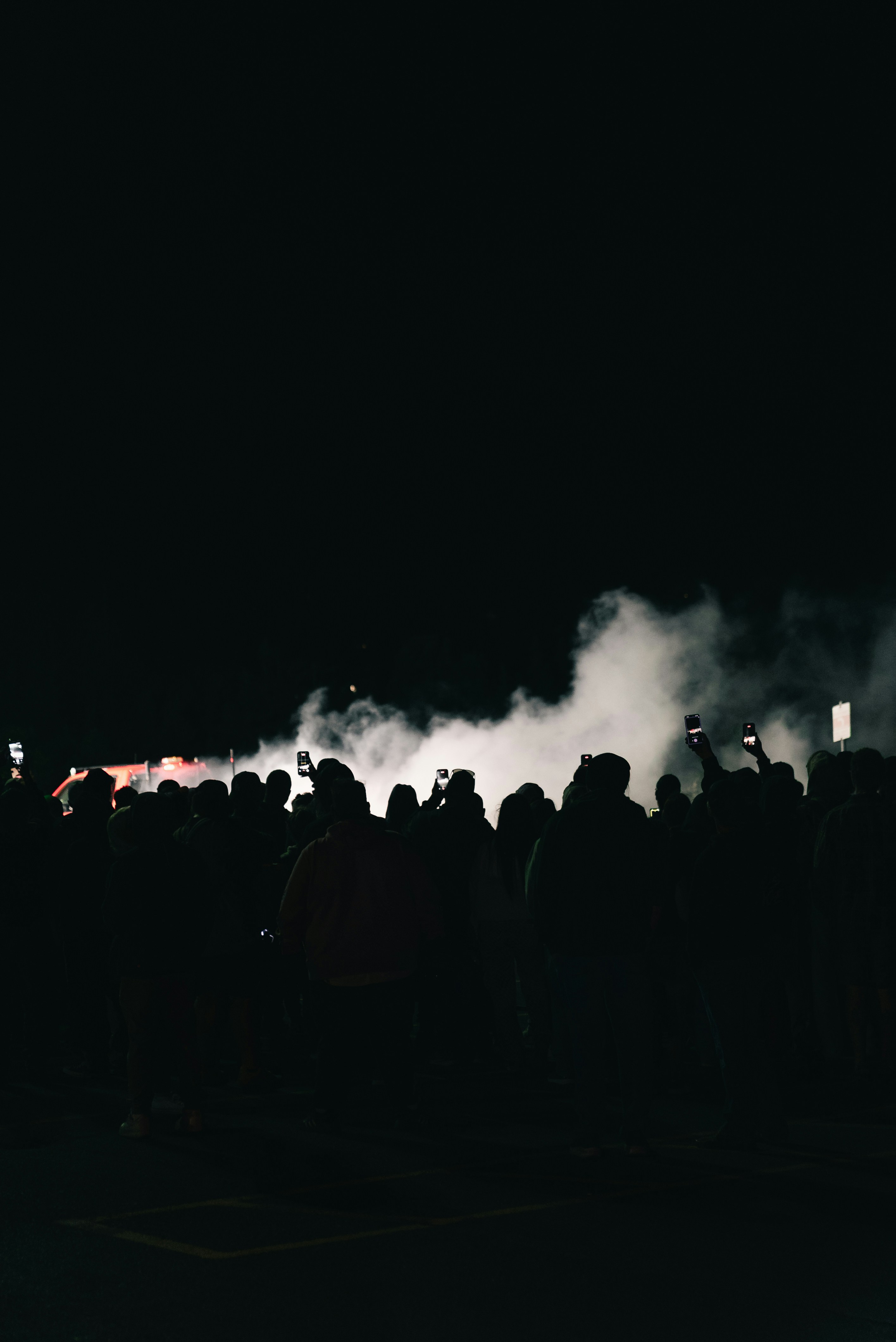 A crowd of people holding up smartphones toward a cloud of thick white smoke