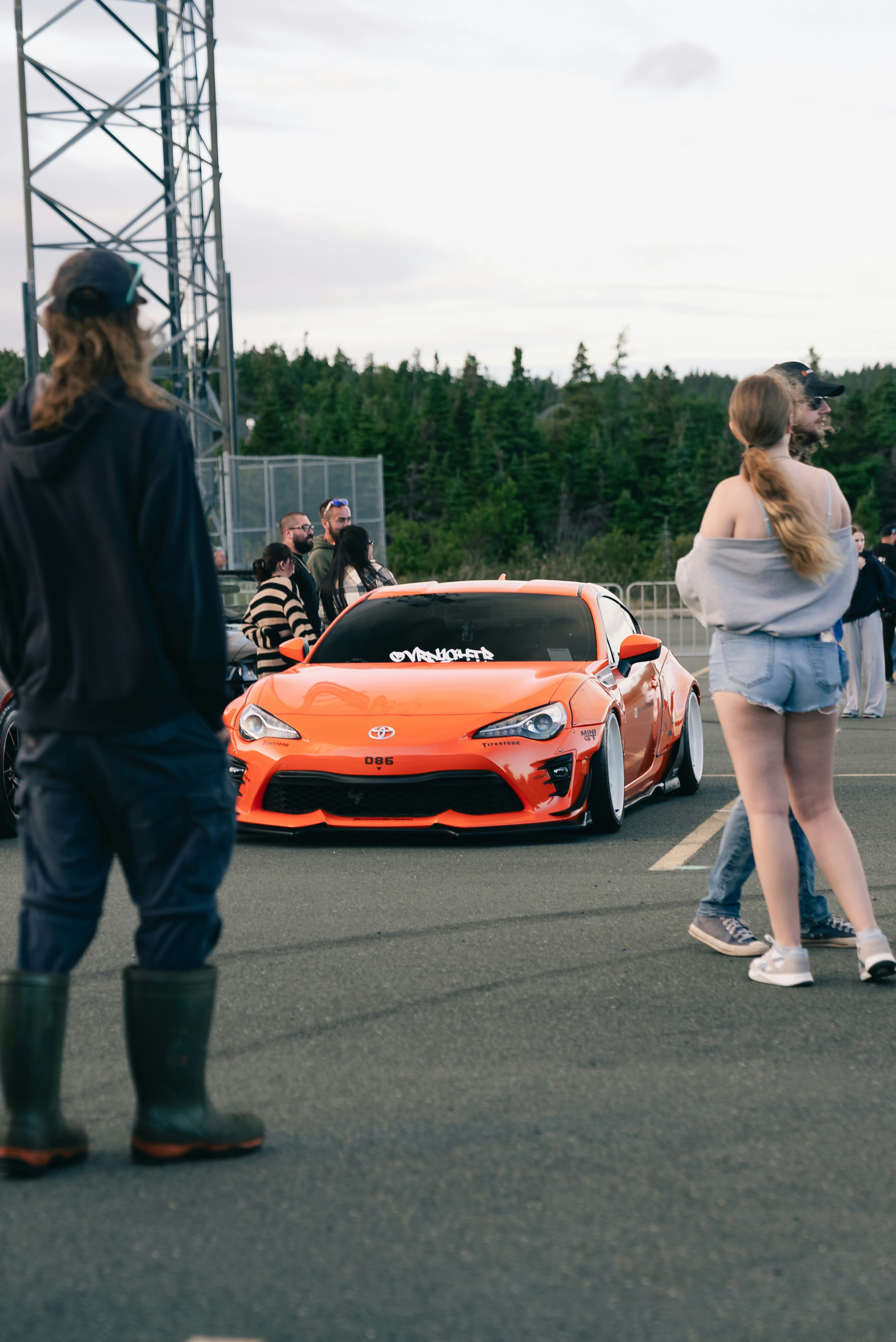 A group of people gathered around a modified orange Toyota sports car outdoors