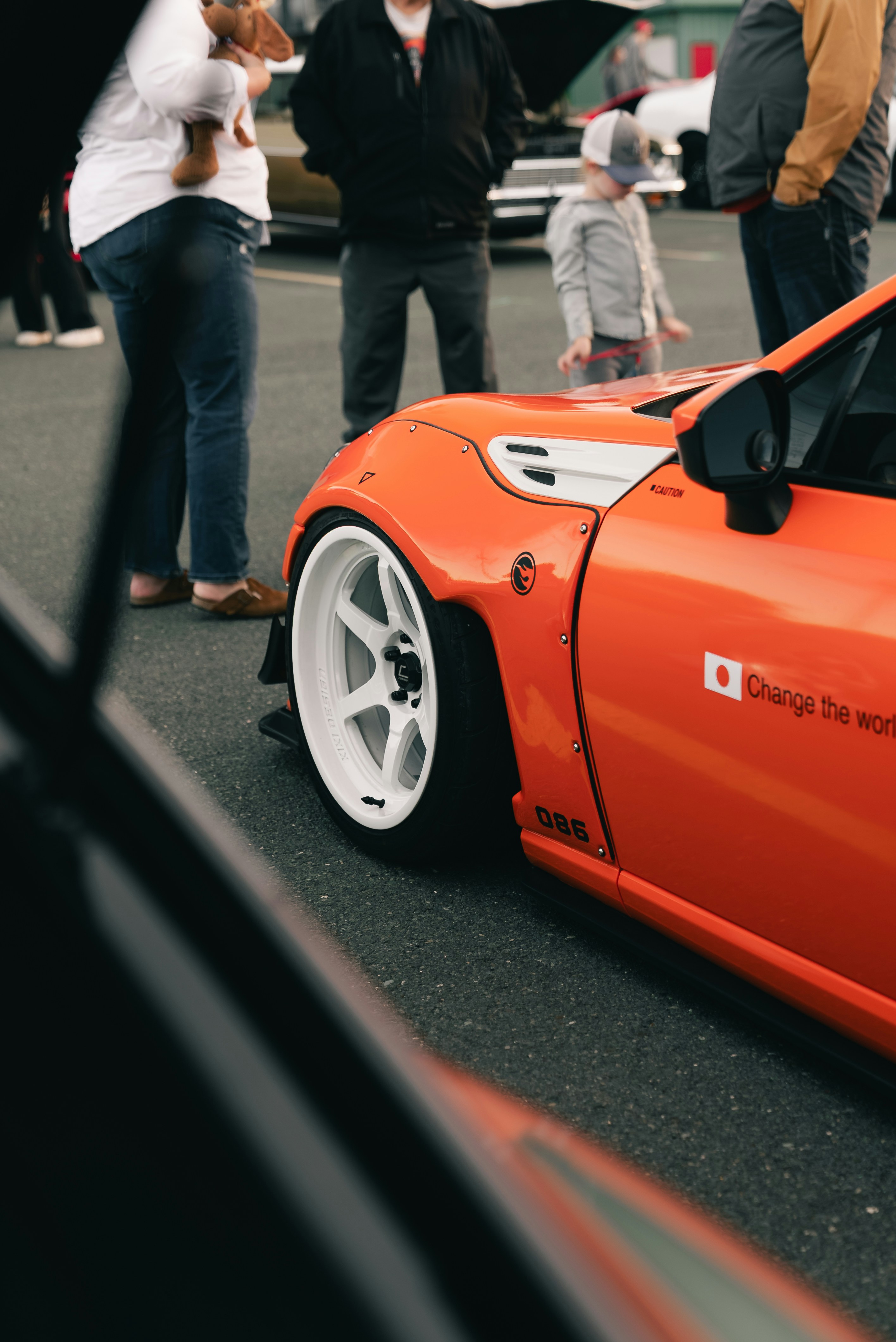 An orange sports car with white rims parked near a group of people
