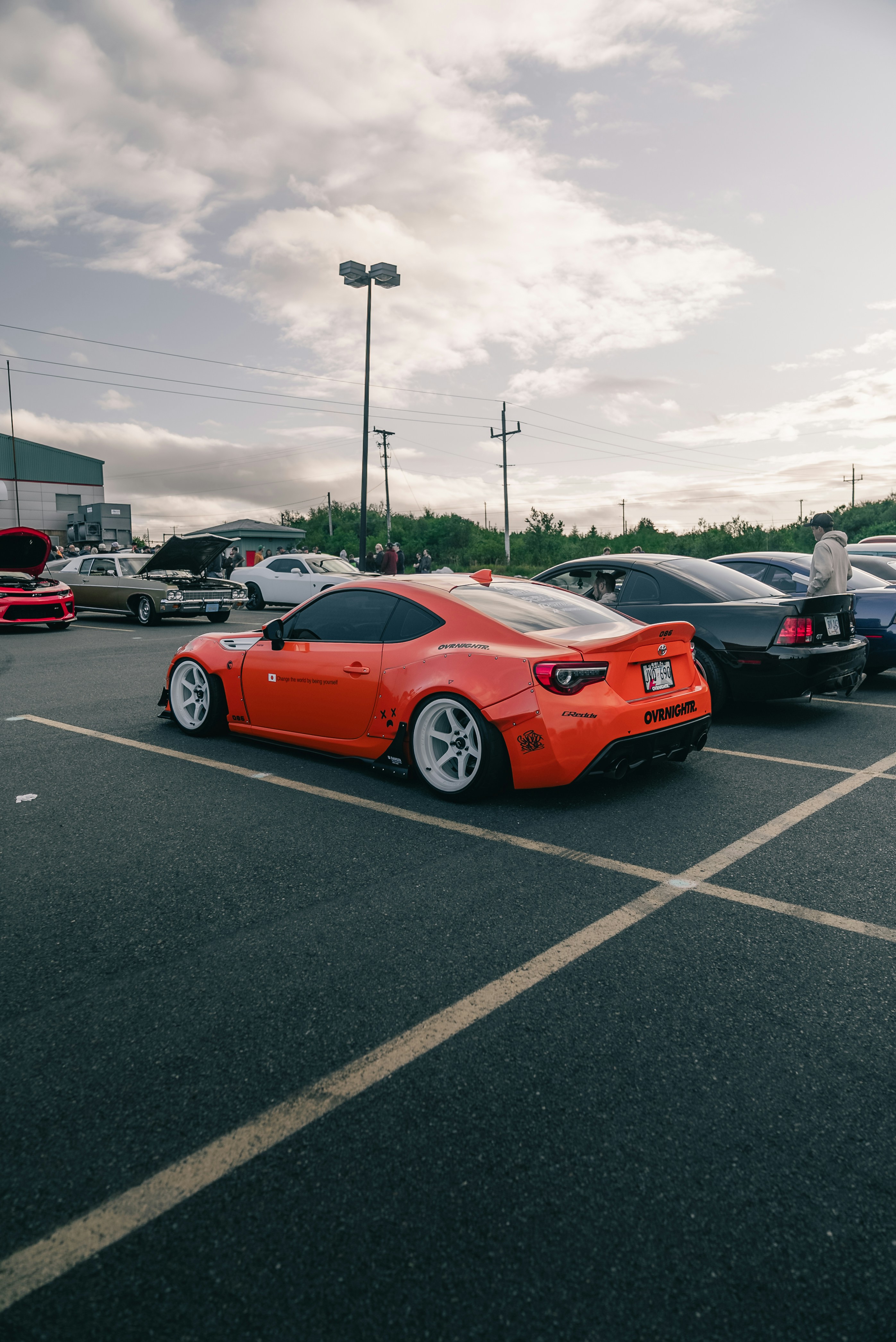 A modified orange sports car with white wheels parked in a paved lot
