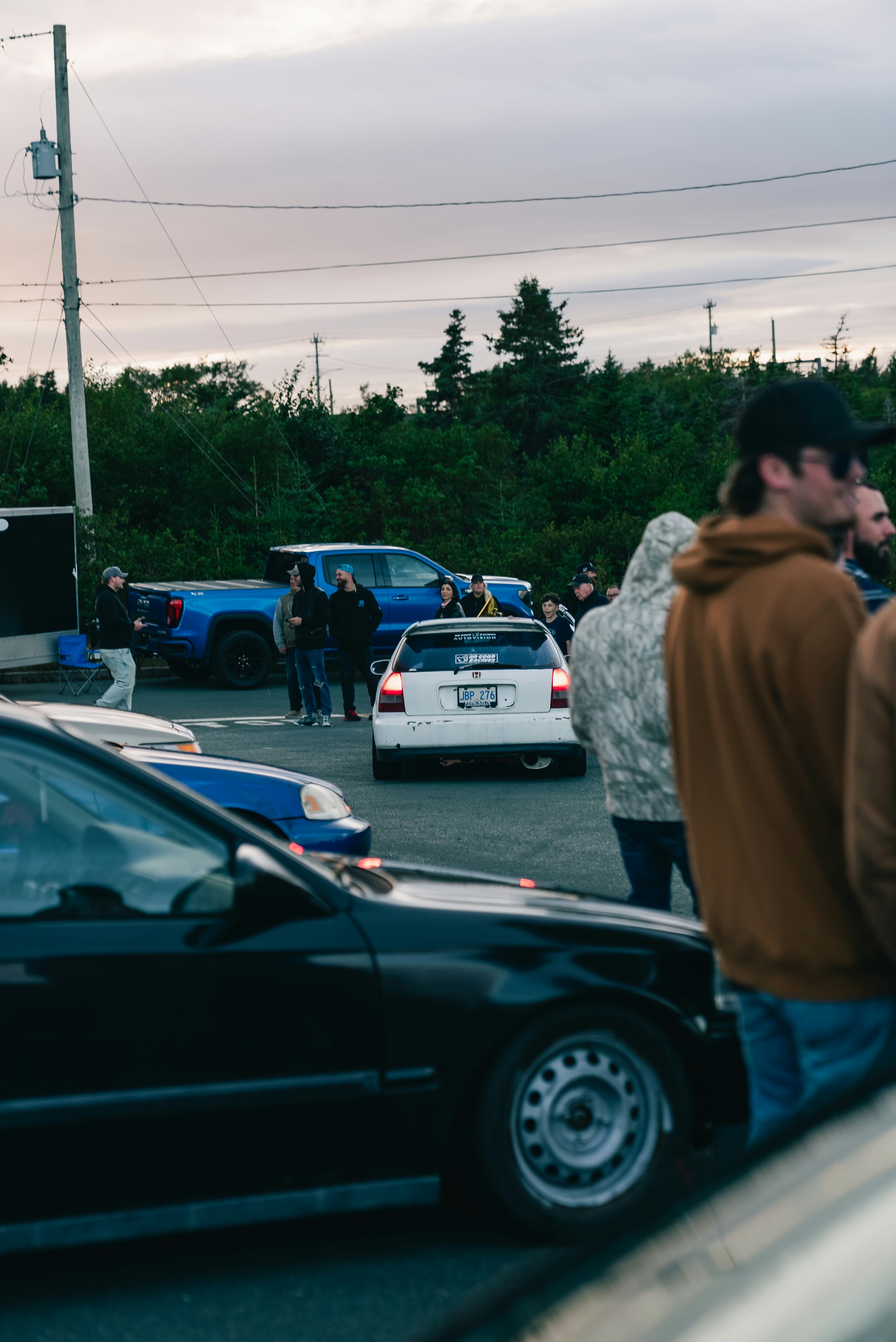 A white hatchback car parked in a lot with people standing nearby