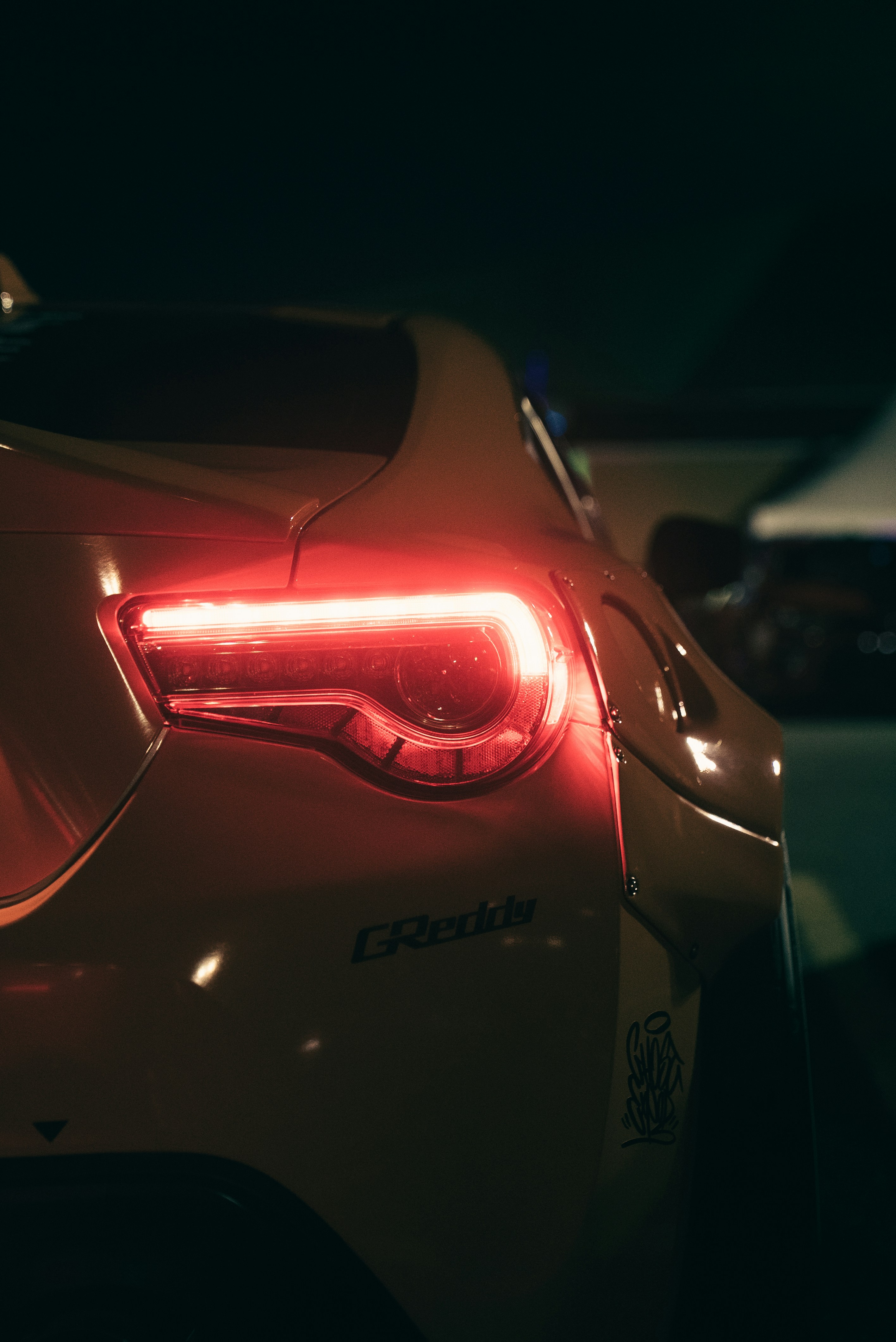 A glowing red taillight on a car with a wide body kit at night