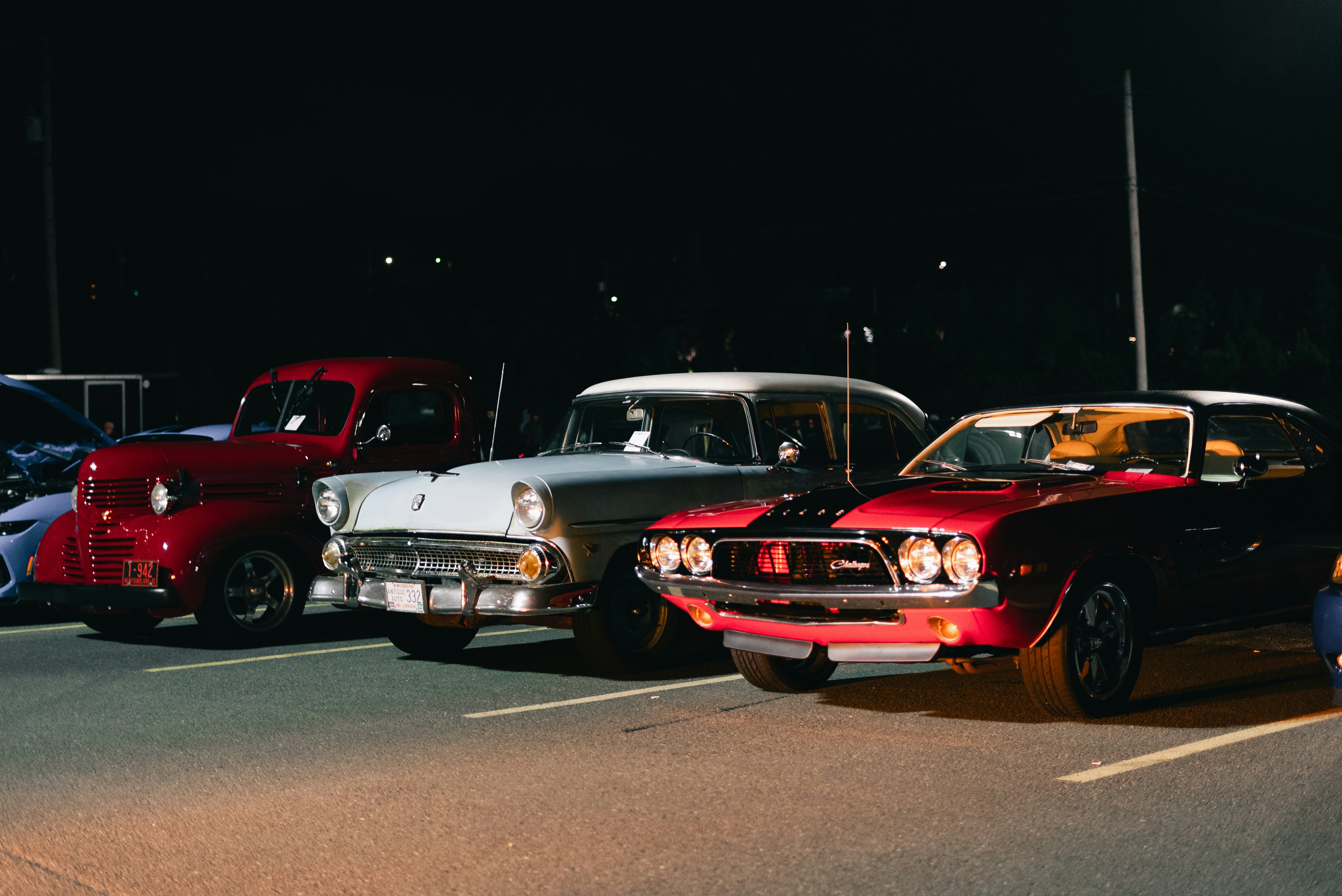 Three classic cars parked in a row on an asphalt lot at night
