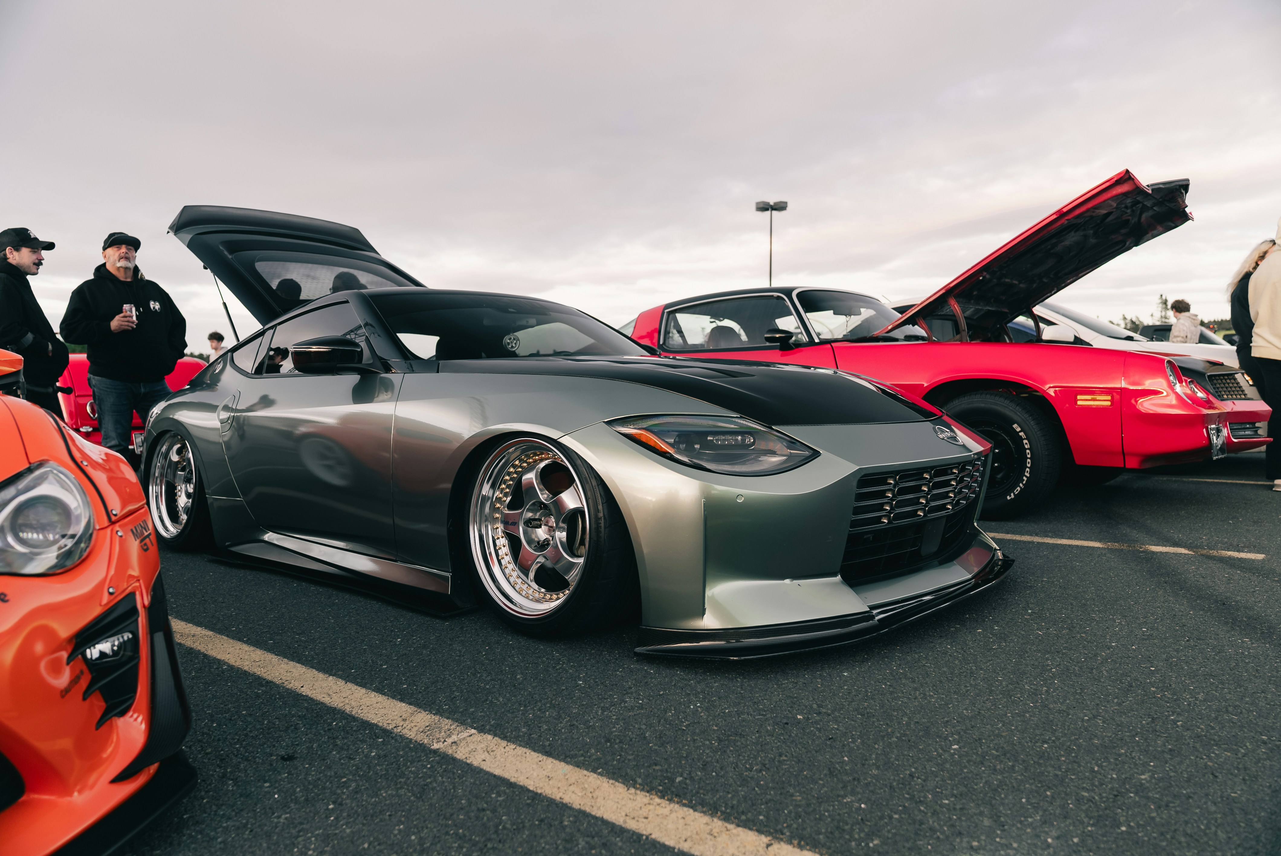 A modified grey sports car with a black hood parked at a car show