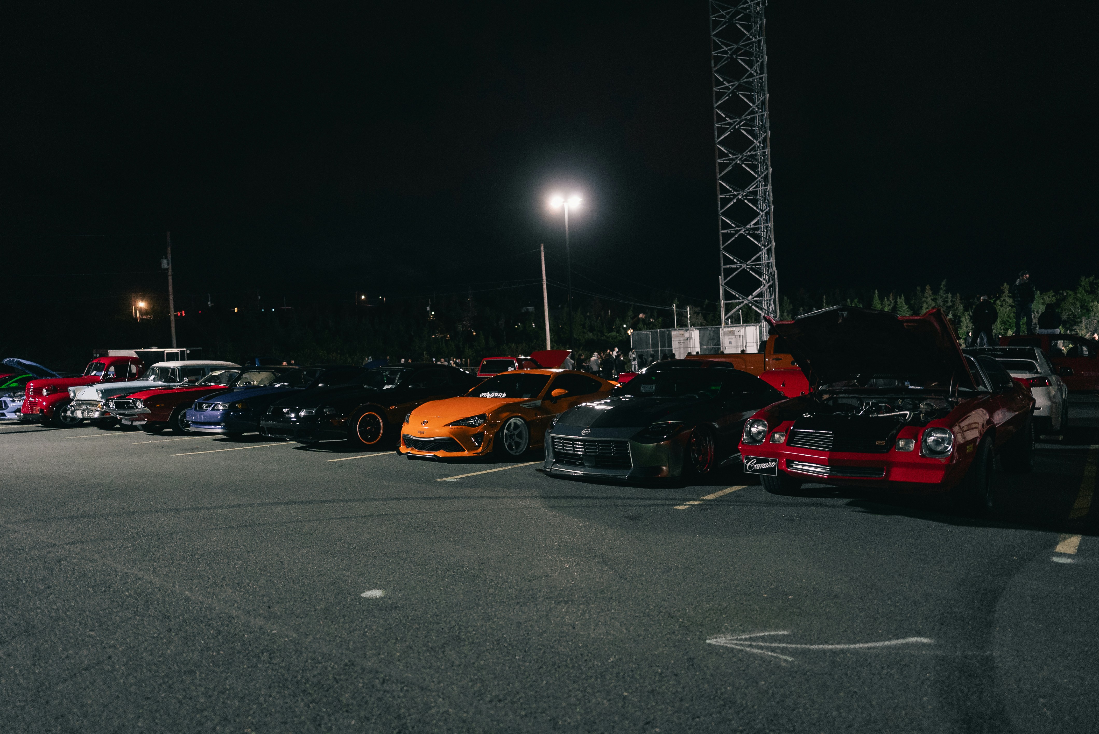 A row of modified sports cars parked in a dark asphalt lot at night