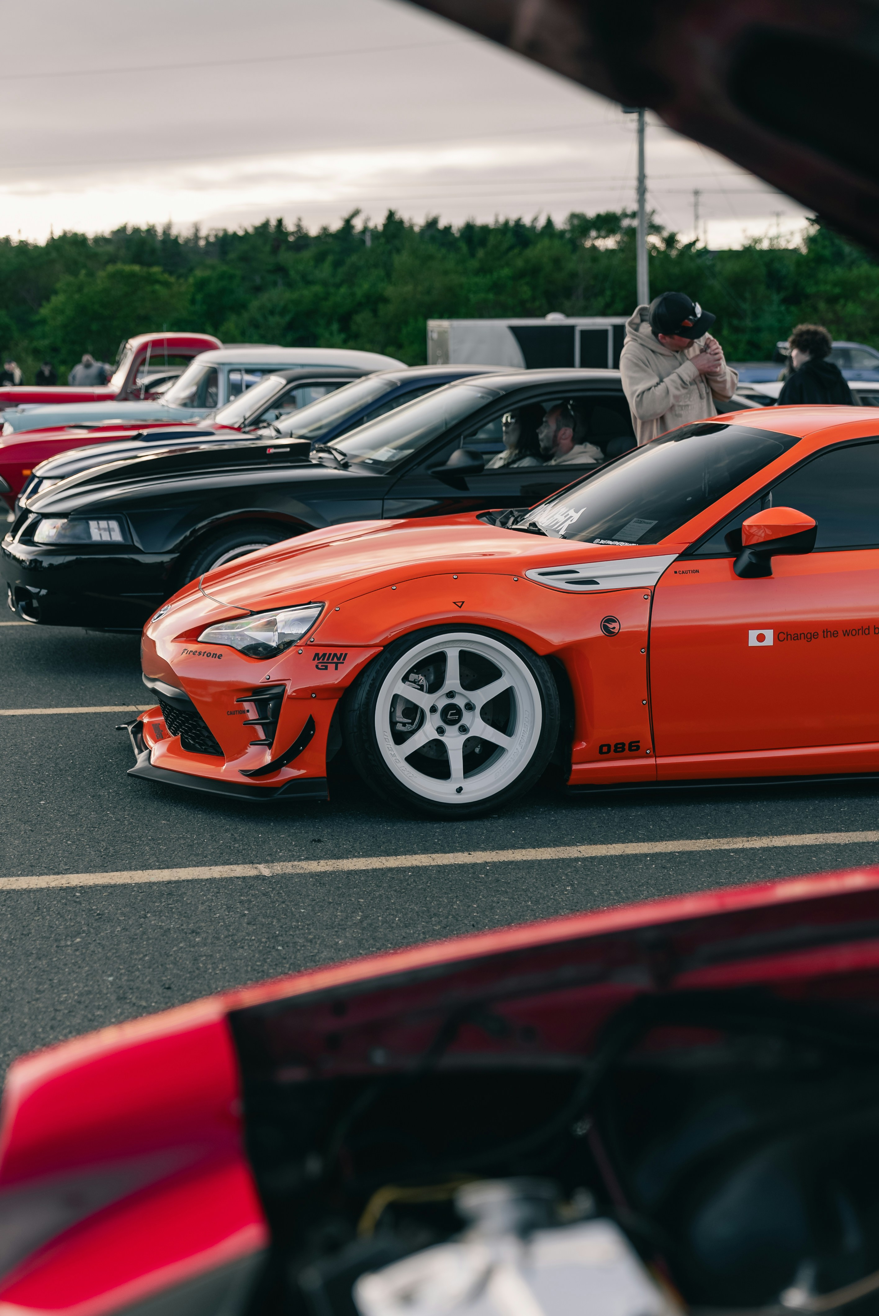 An orange modified sports car parked in a row of vehicles at a meet