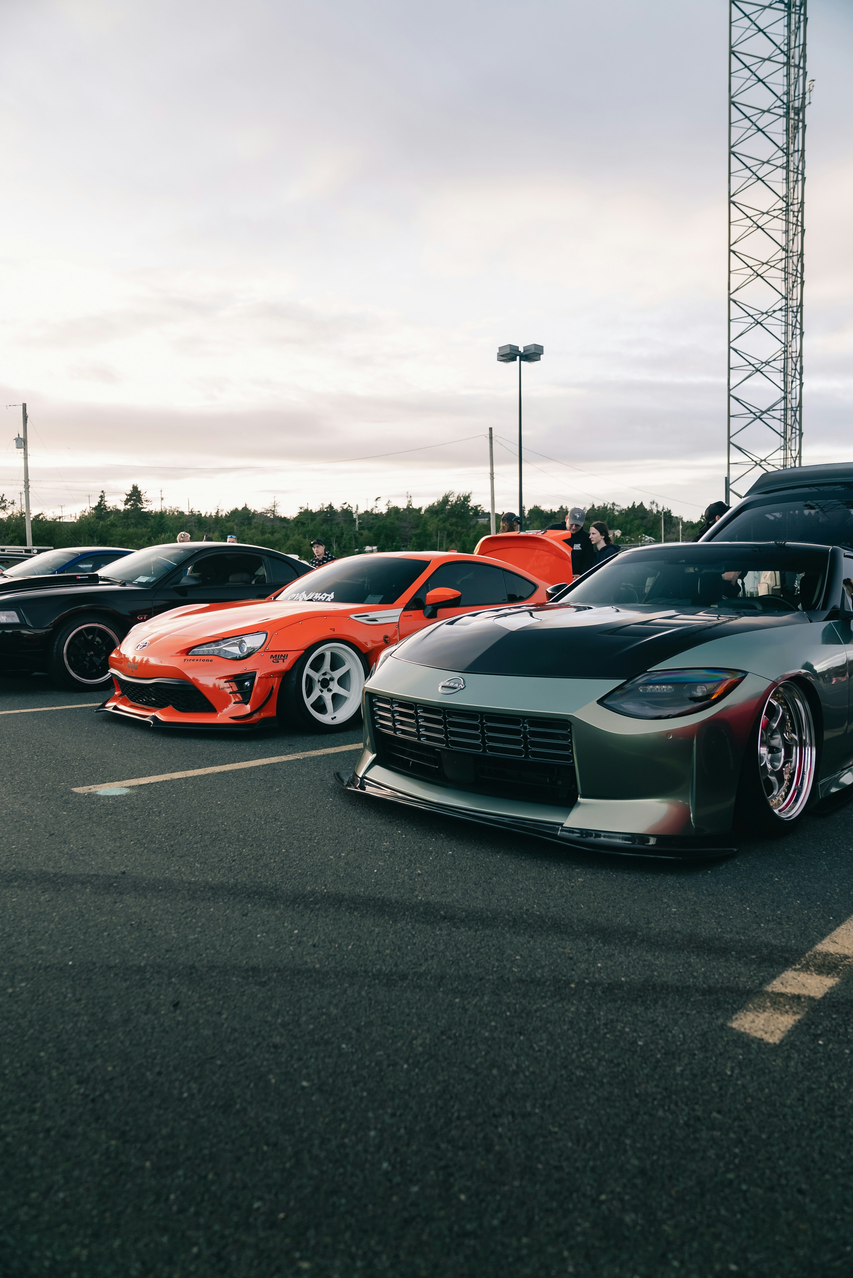 Modified sports cars parked in a row at an outdoor car meet