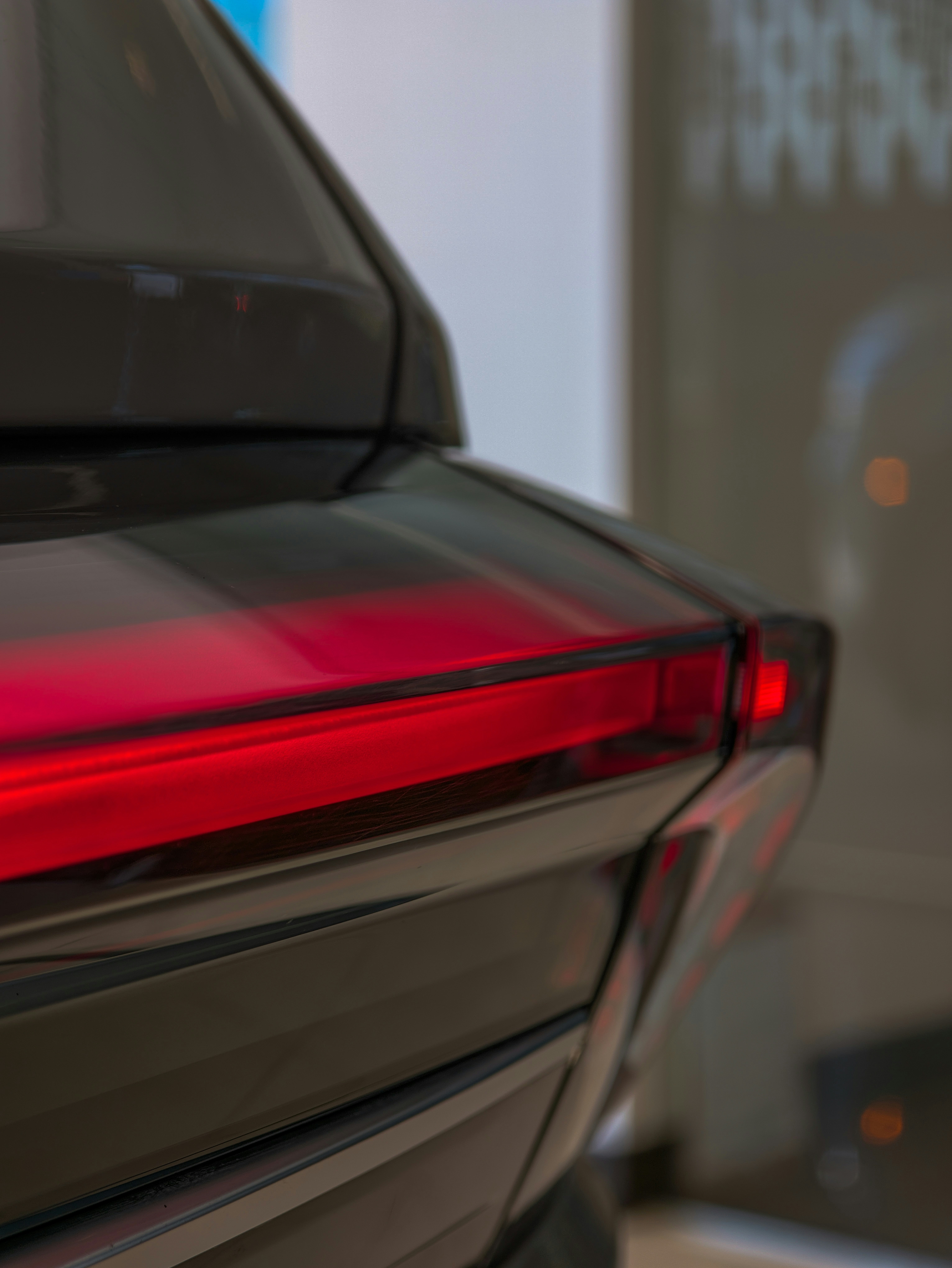 A close-up reveals a sleek, horizontal red LED taillight slicing through the glossy black exterior of a modern vehicle, highlighting sharp aerodynamic contours, polished glass, and deep, dark metallic reflections.