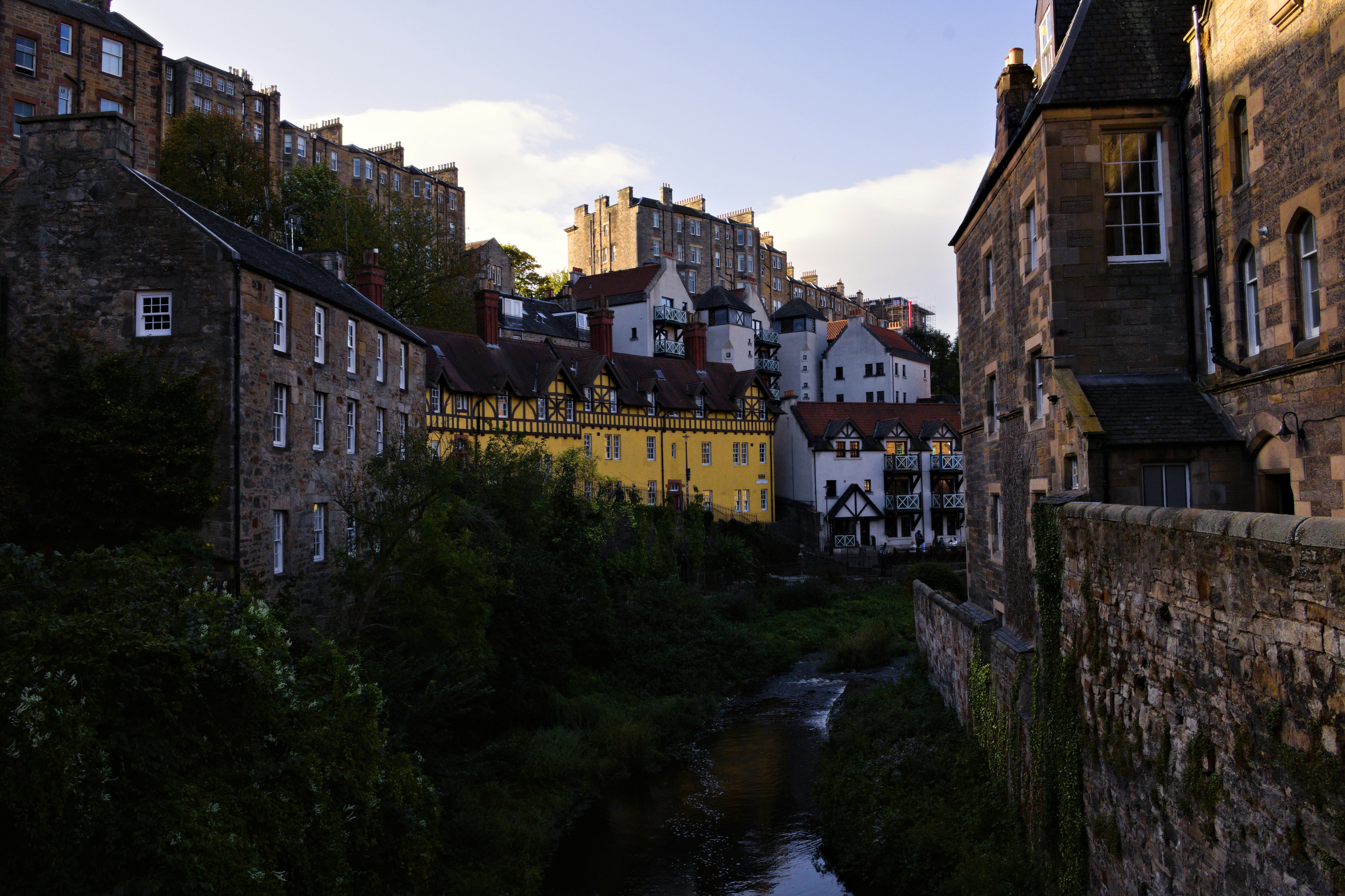 A narrow river flowing between stone buildings and a yellow timber-framed house in Edinburgh