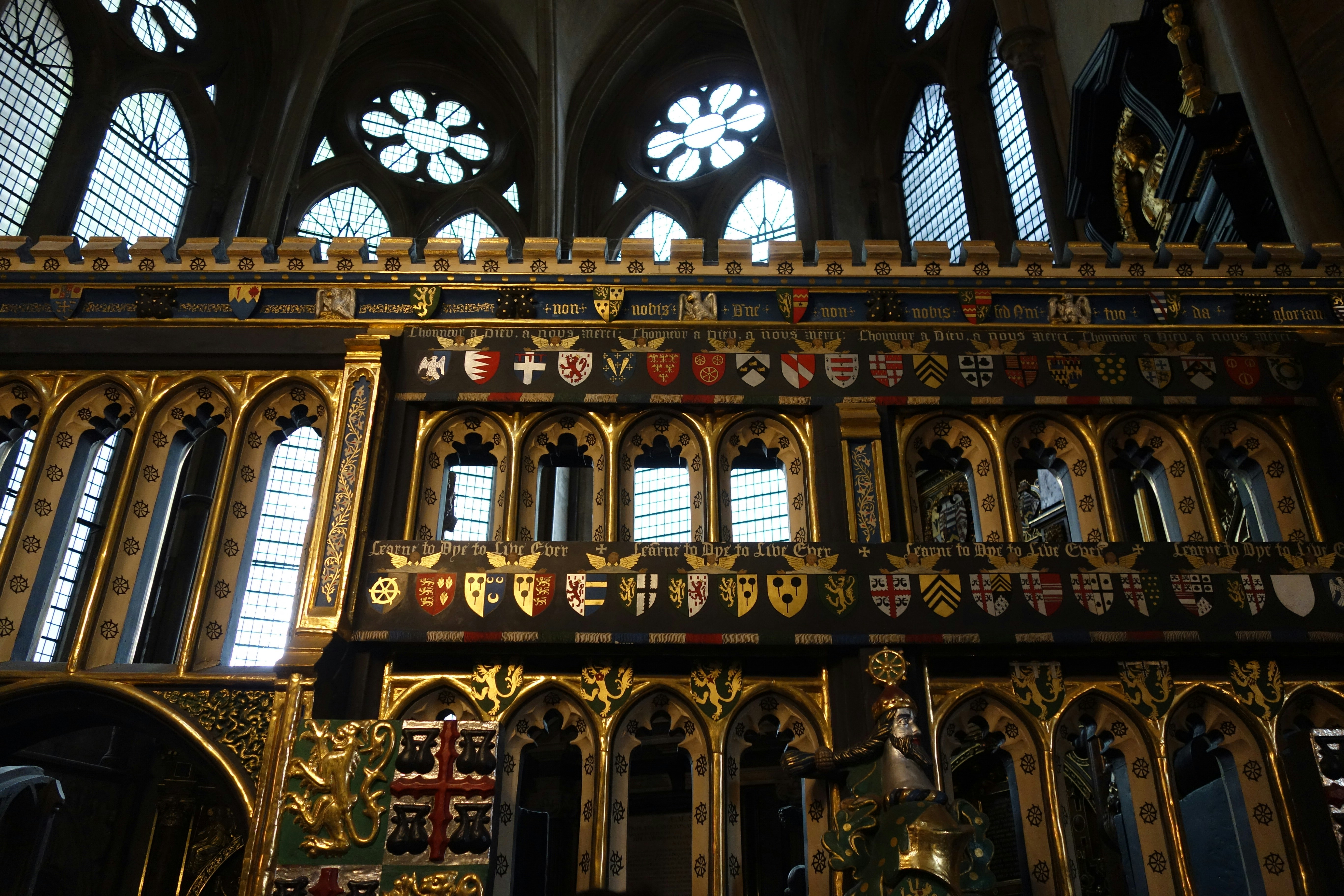 Fileiras de escudos heráldicos coloridos sobre uma grade de madeira dourada e preta em uma igreja