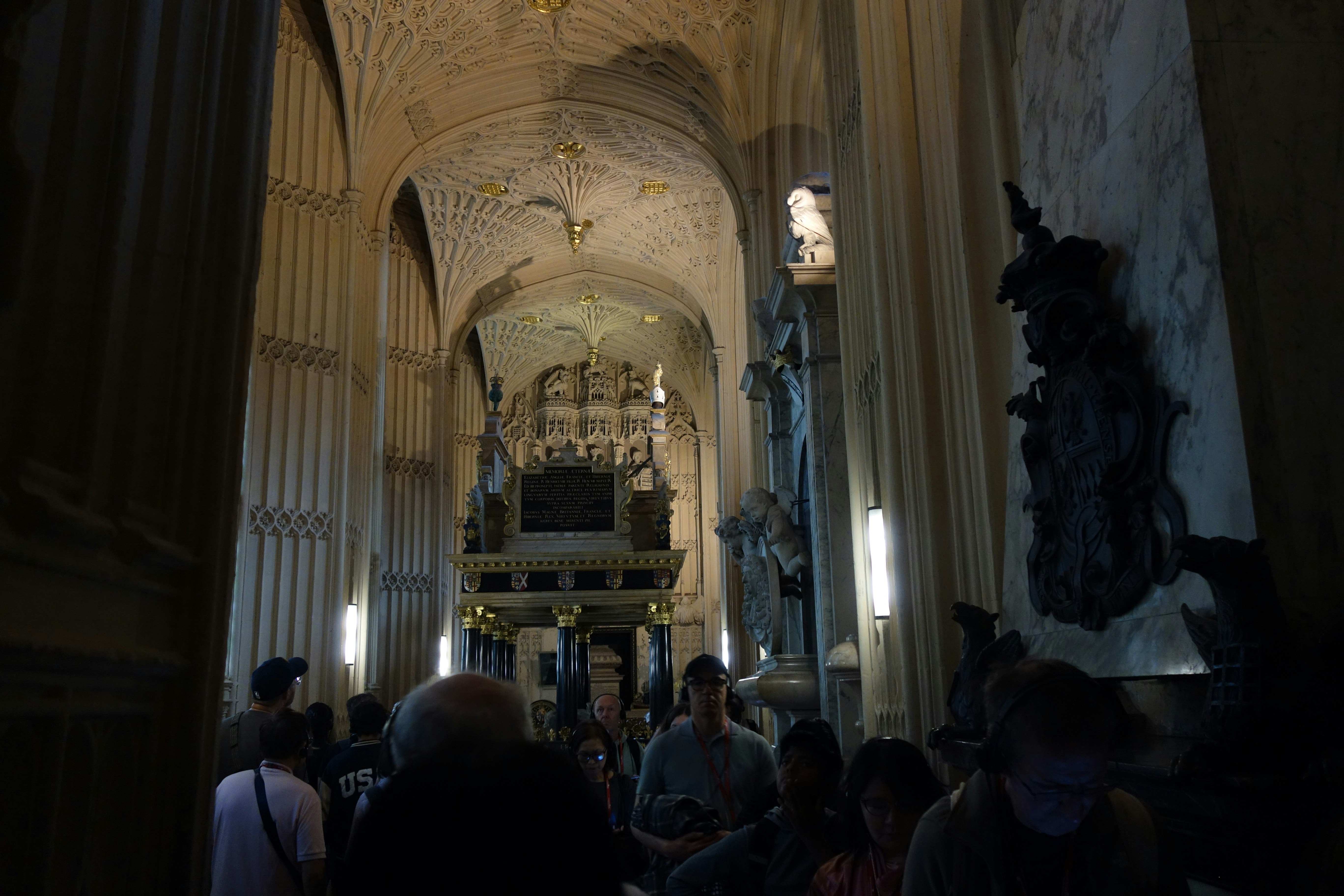 Um grupo de pessoas caminhando por uma catedral de pedra com teto abobadado ornamentado