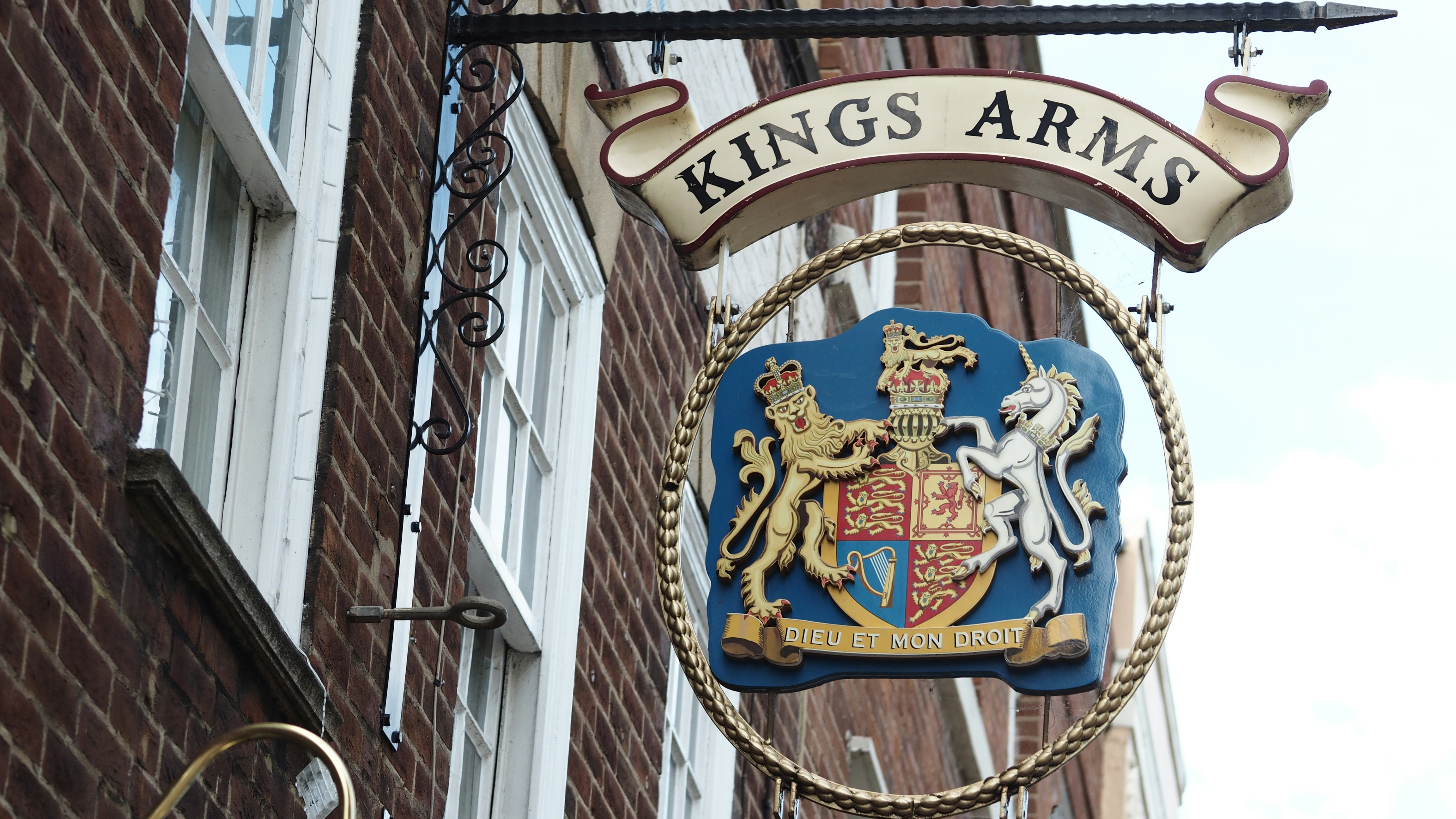 Uma placa pendurada com as palavras King's Arms com um brasão real sobre tijolos