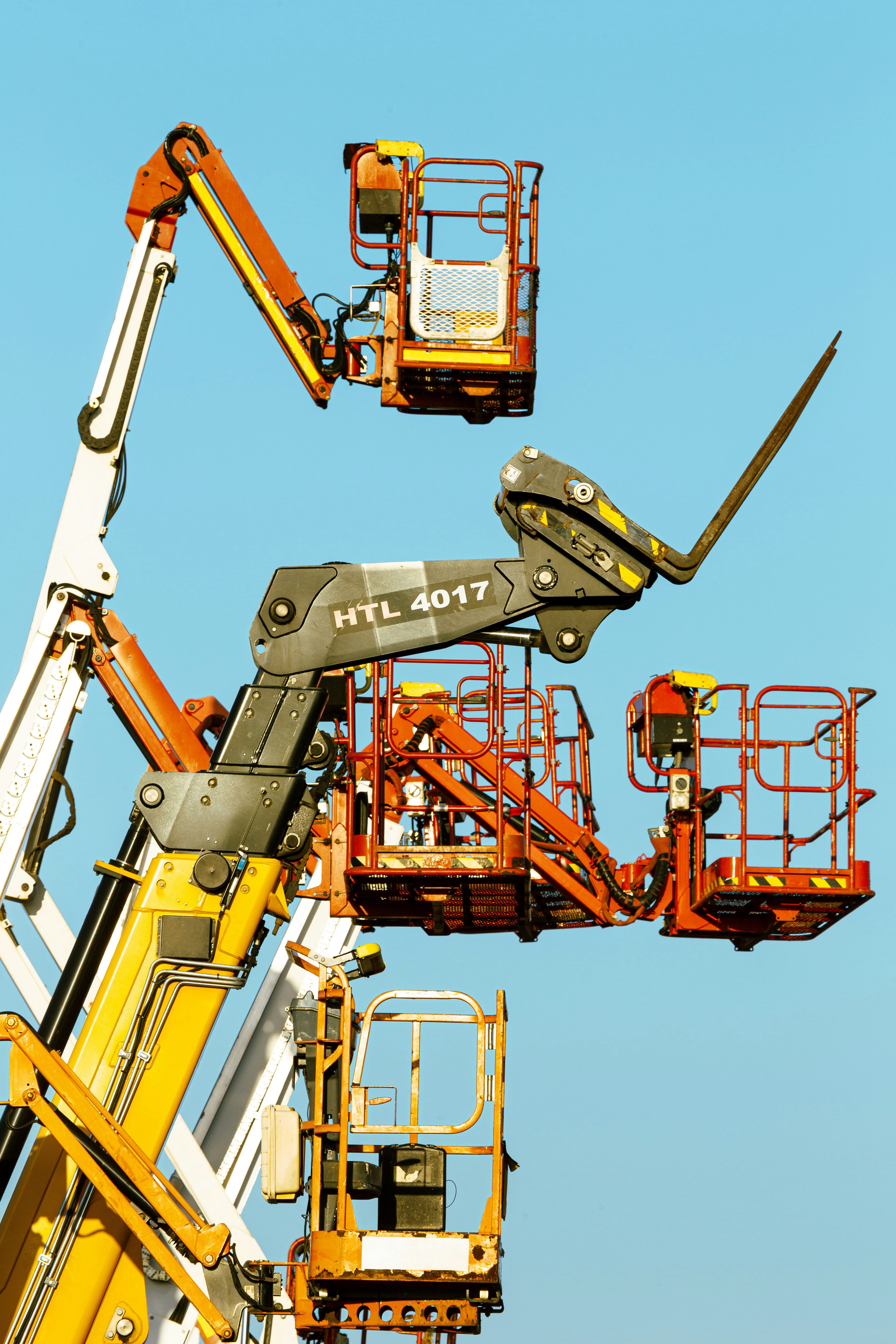 Three orange and yellow aerial work platforms against a clear blue sky