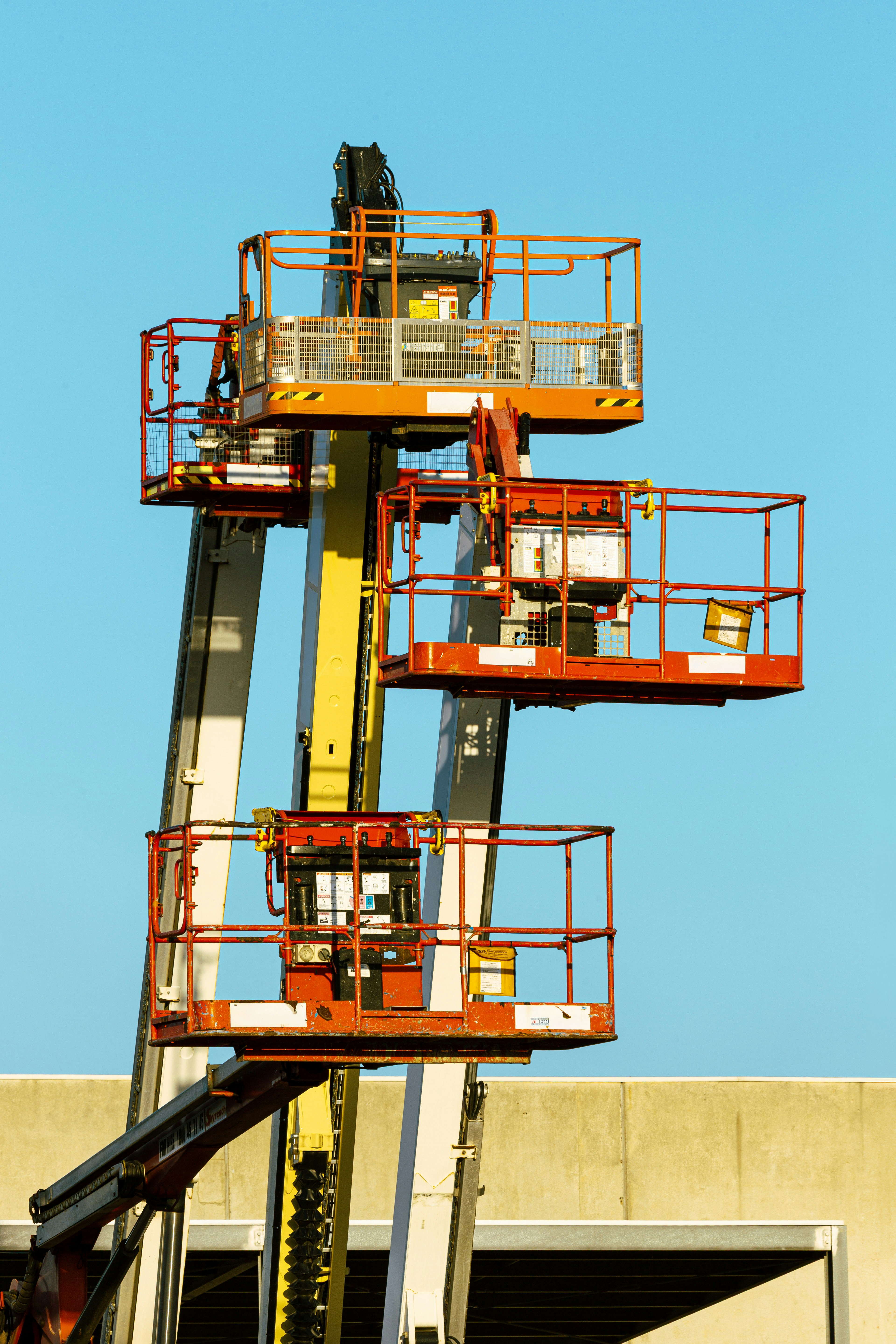 Three orange aerial work platforms extended against a clear blue sky