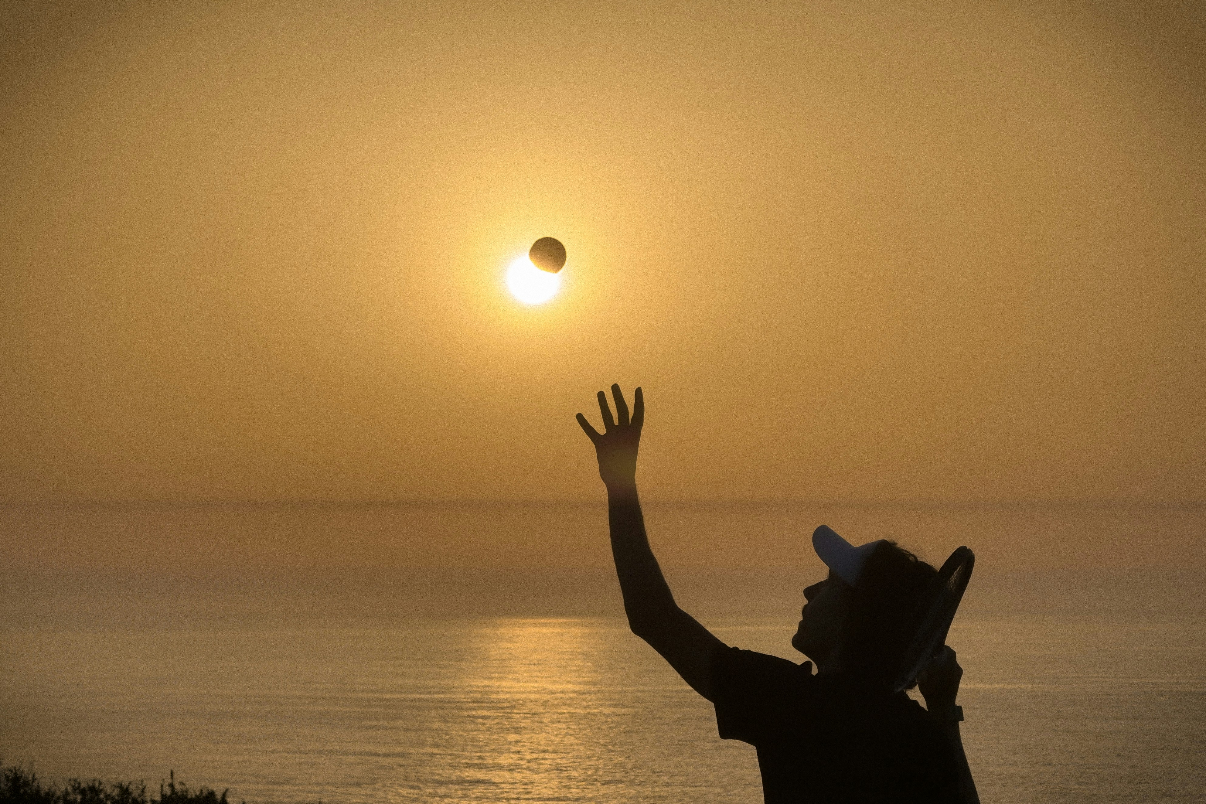 A person in silhouette tossing a tennis ball against a warm orange sky