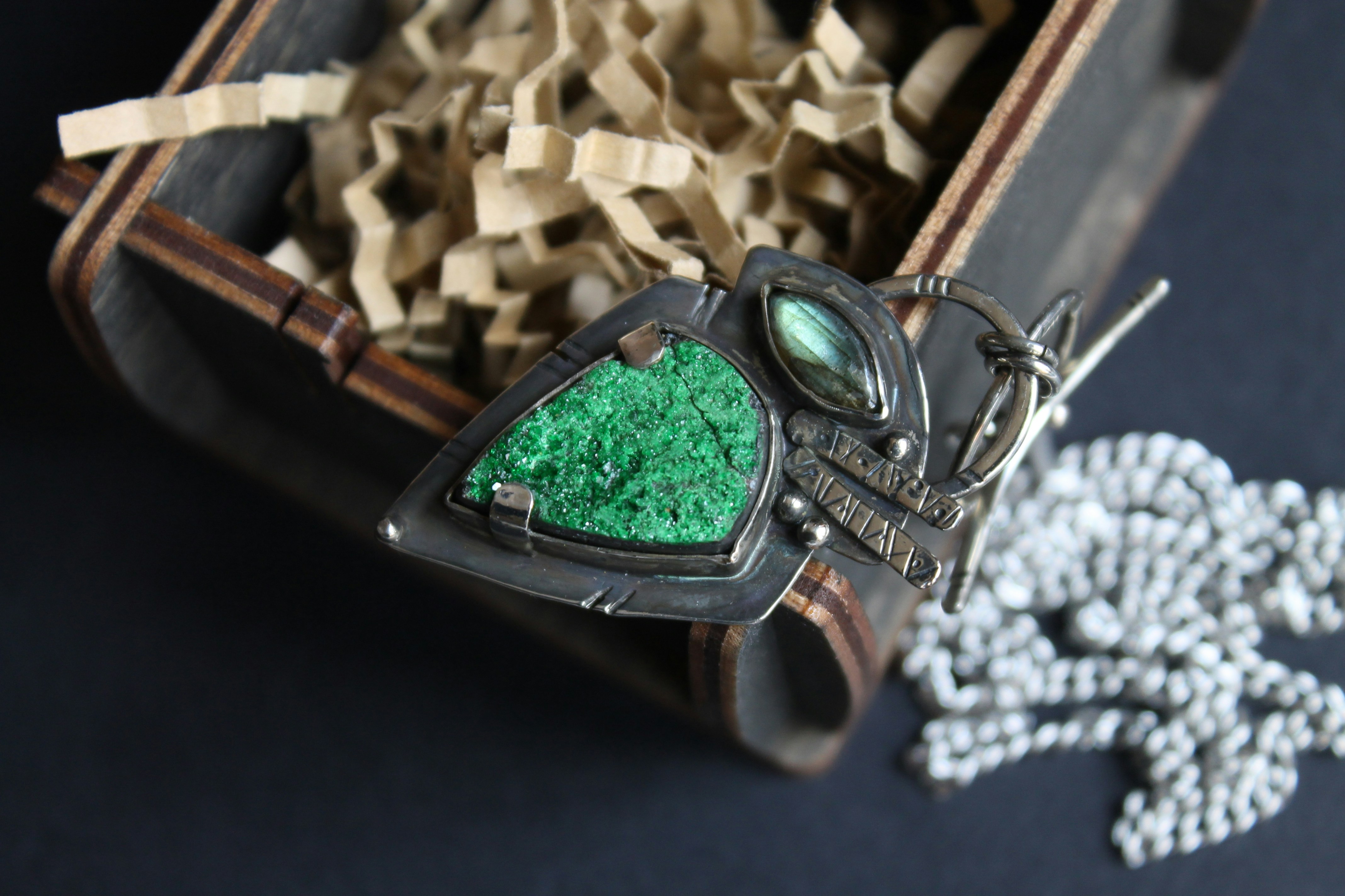 A silver pendant with a green druzy stone and labradorite in a wooden box