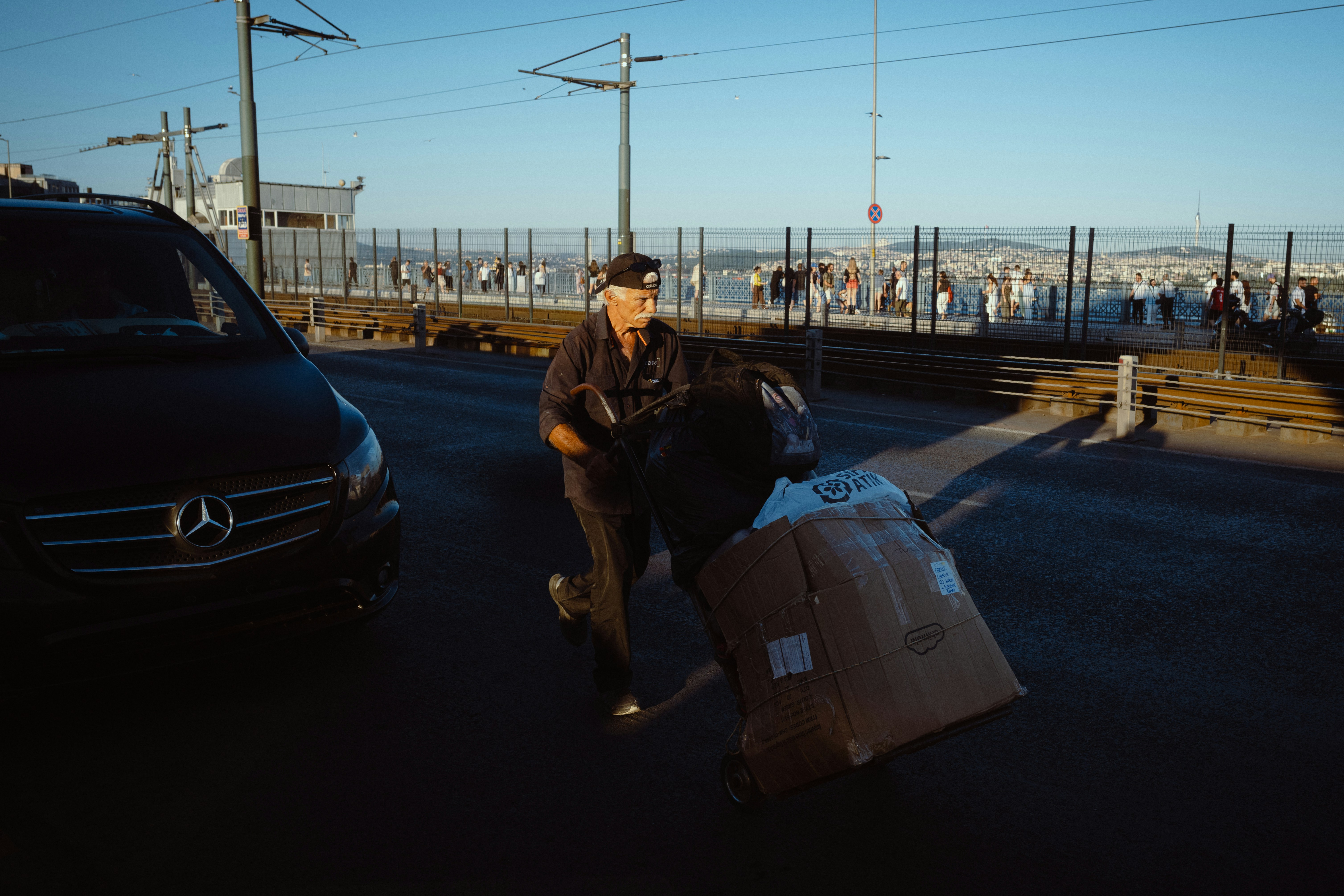 A man pushing a cart loaded with cardboard boxes on a city bridge