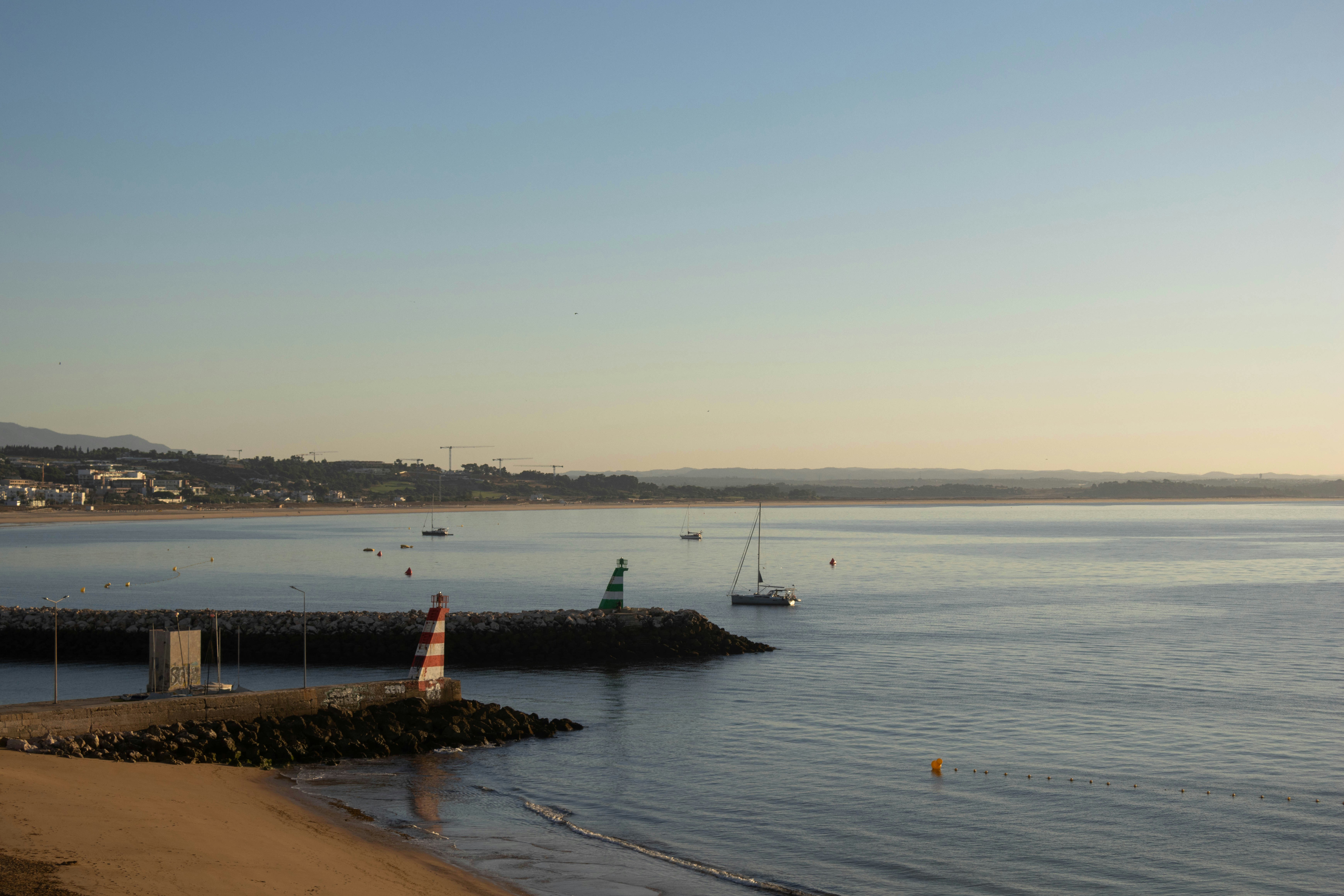 A red and white lighthouse on a stone jetty in a calm bay