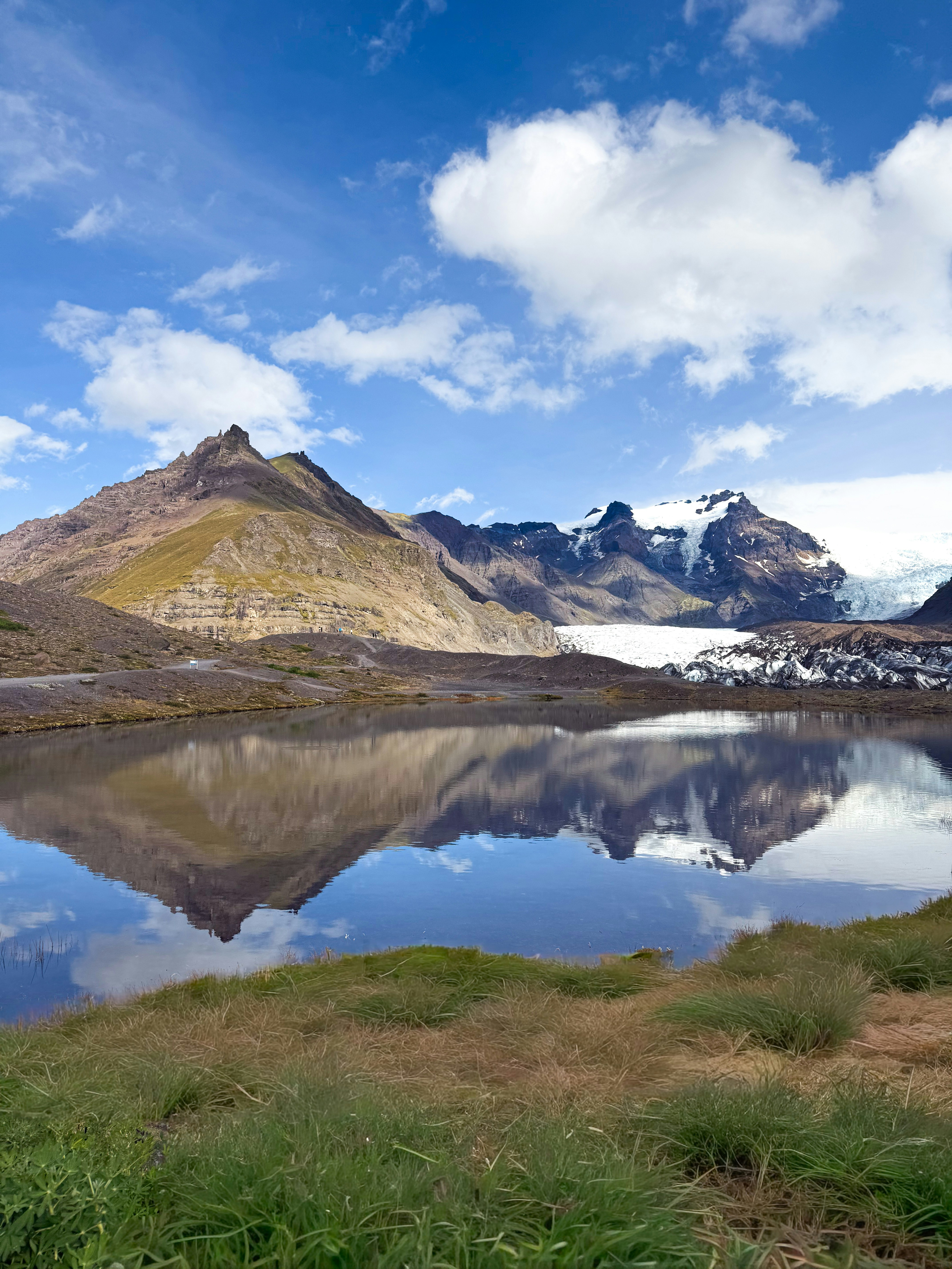 Um lago glacial refletindo montanhas cobertas de neve e um céu azul com nuvens