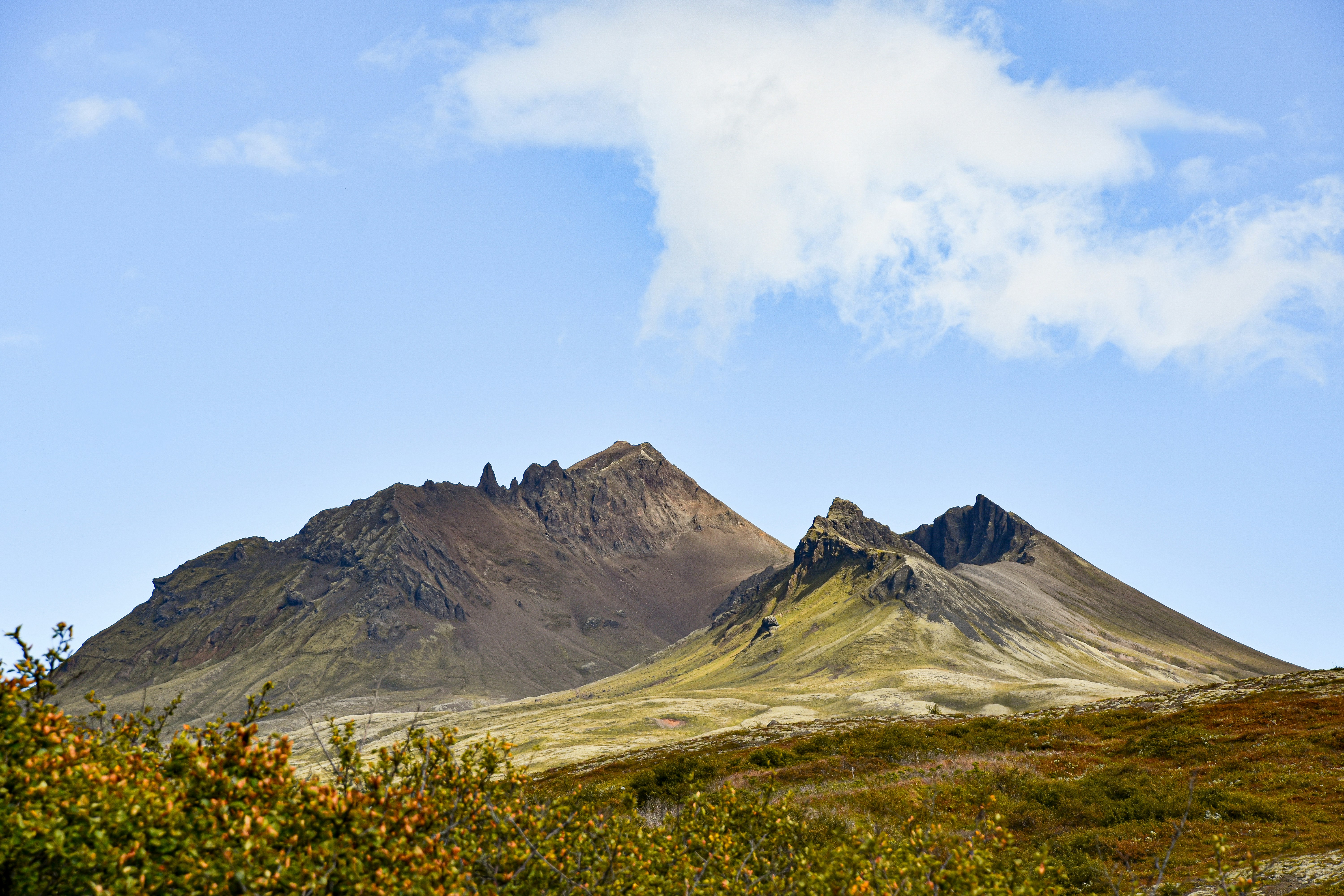 Picos montanhosos marrons e acidentados se erguendo acima de uma paisagem verde-musgosa sob um céu azul