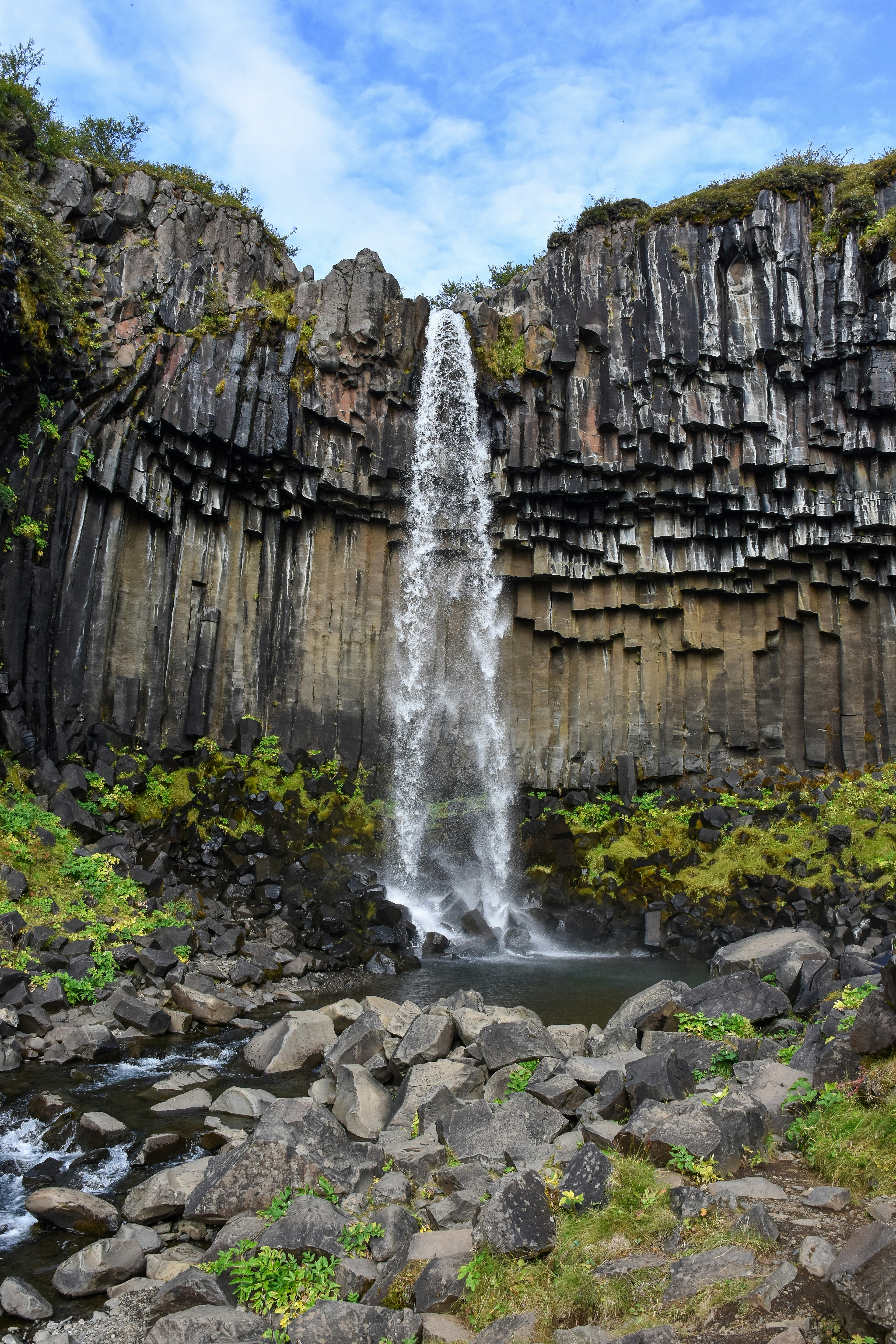 Uma cachoeira caindo sobre colunas de basalto escuro até uma piscina rochosa na Islândia