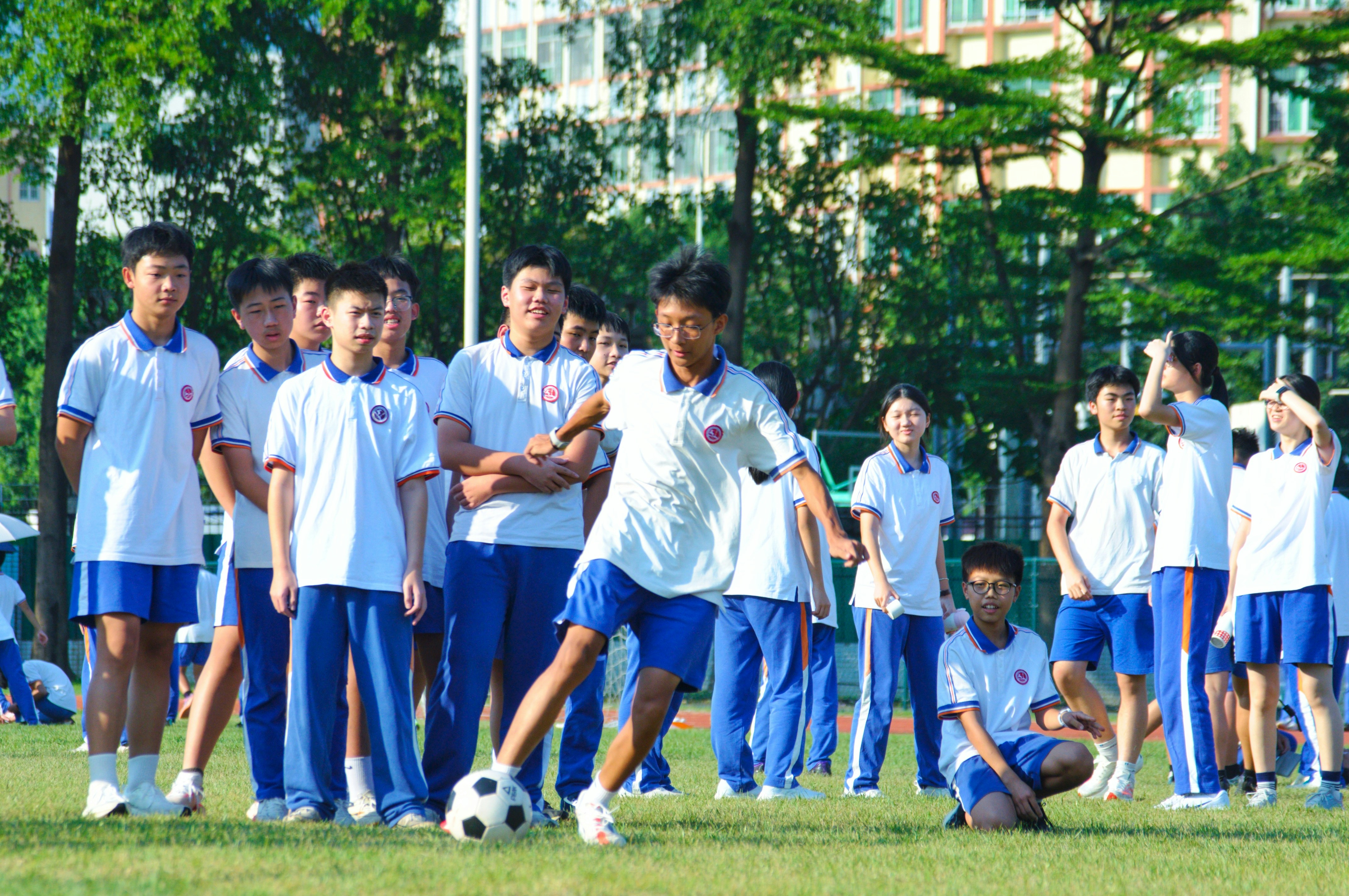 A group of students in white and blue uniforms playing soccer on a field