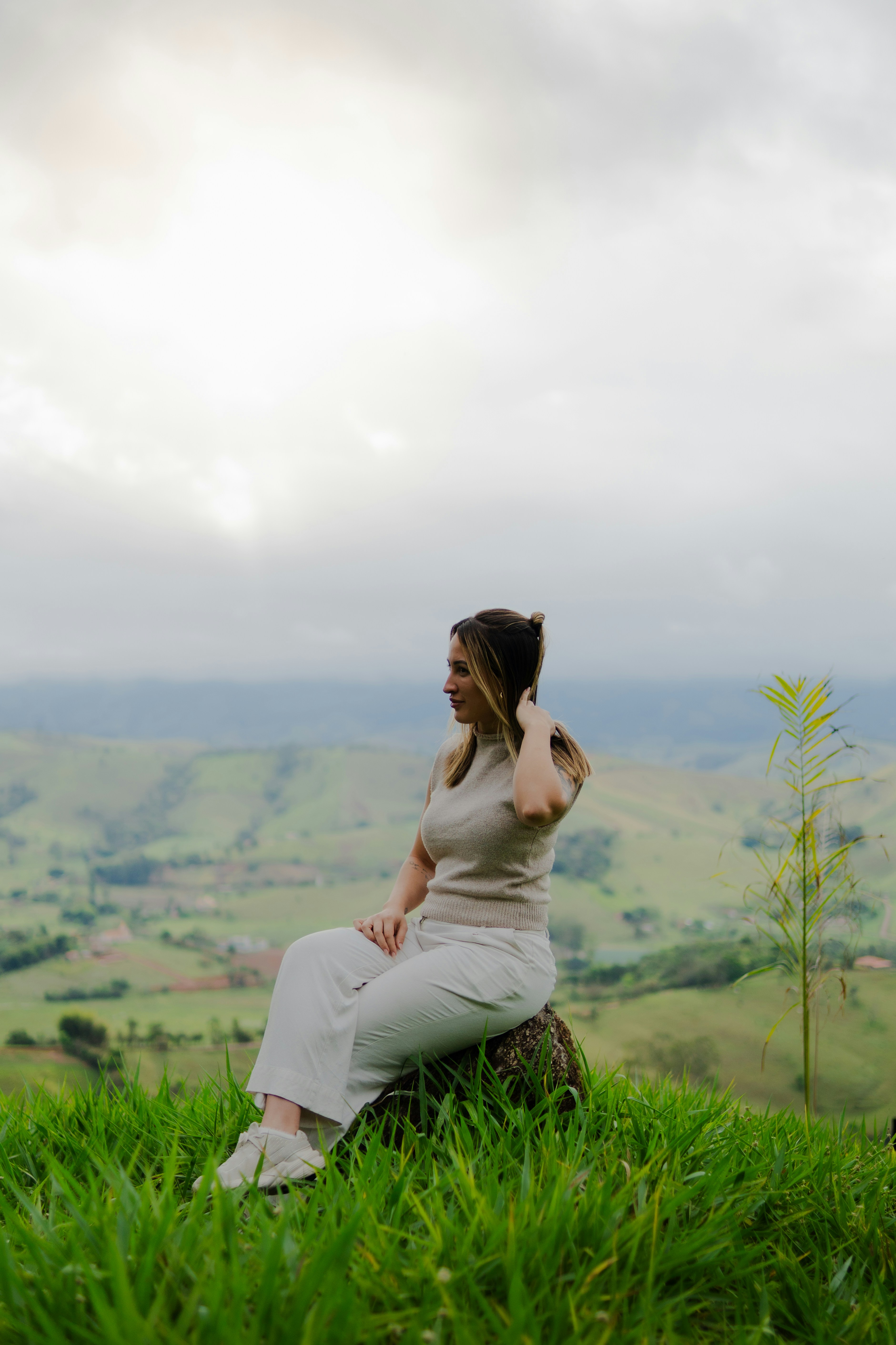 A woman in a beige top and white pants on a grassy hill