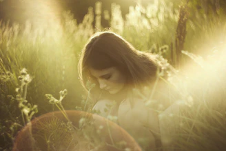 A woman crouching in tall grass during golden hour with a terracotta pot