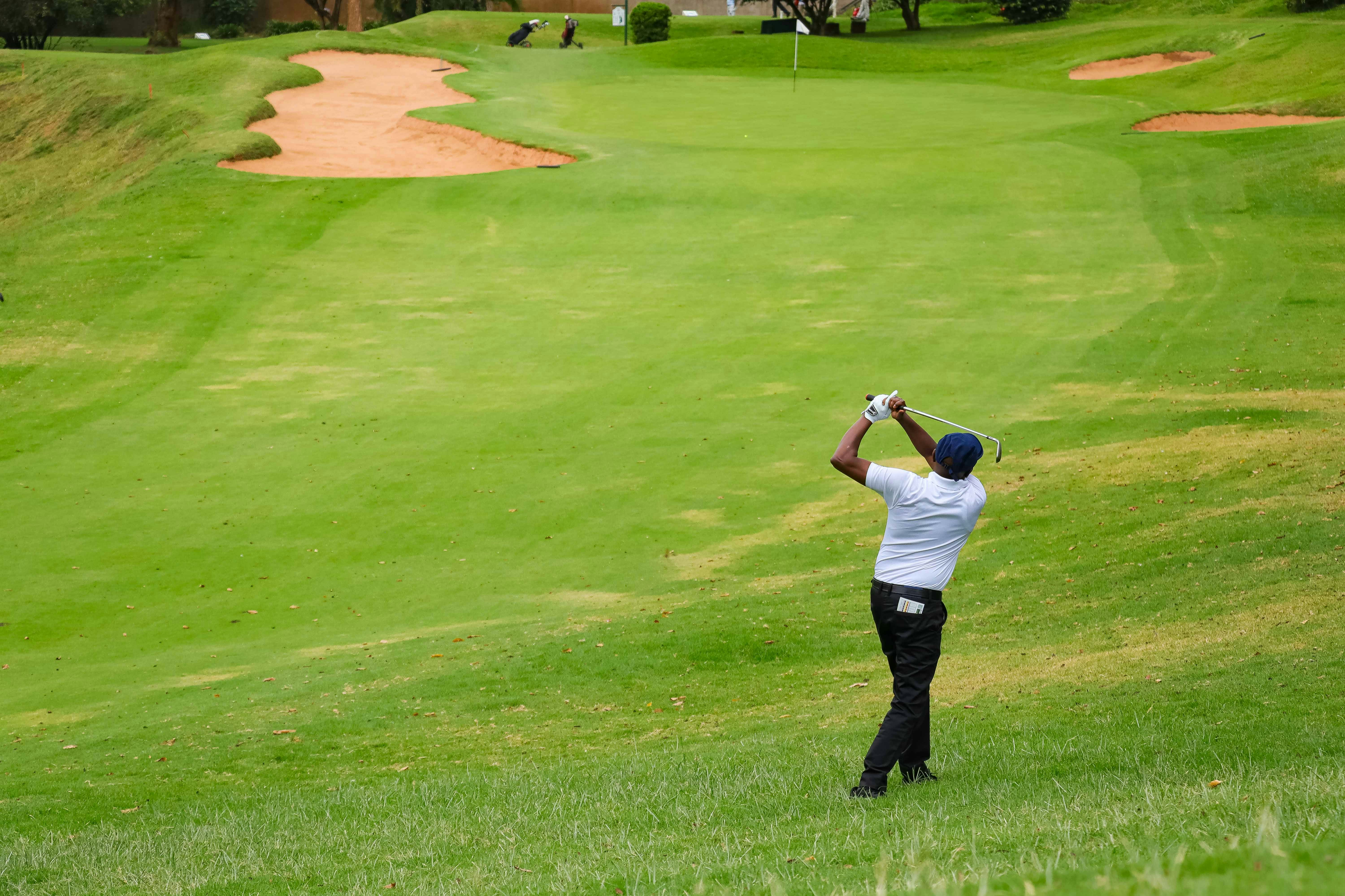 A golfer in a white shirt swinging a club on a green golf course
