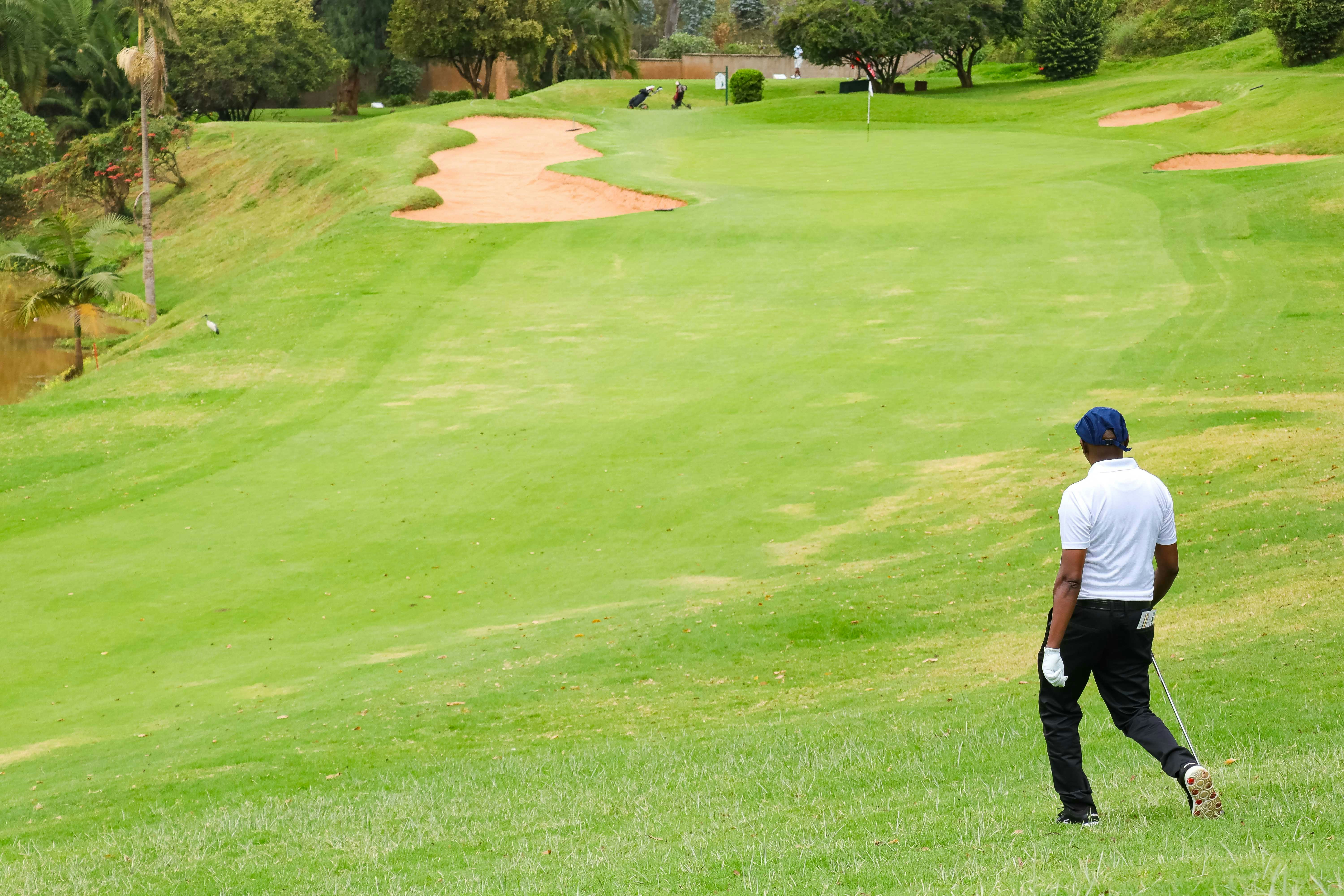 A golfer in a white shirt and blue cap walking on a green course